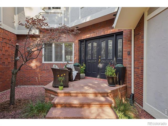 Brick home entry with black double doors, raised patio seating, and potted plants.