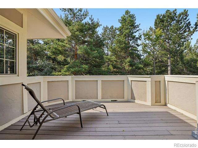Outdoor deck with a dark reclining chair and pine trees beyond the cream railing.