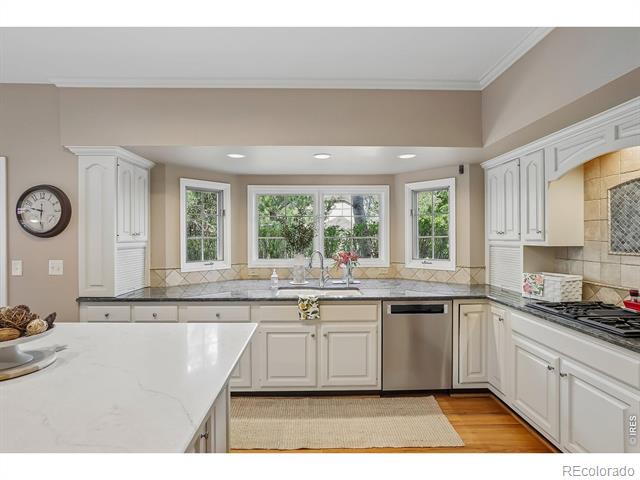 Bright white kitchen with stone counters, bay windows, stainless appliances, and hardwood flooring.