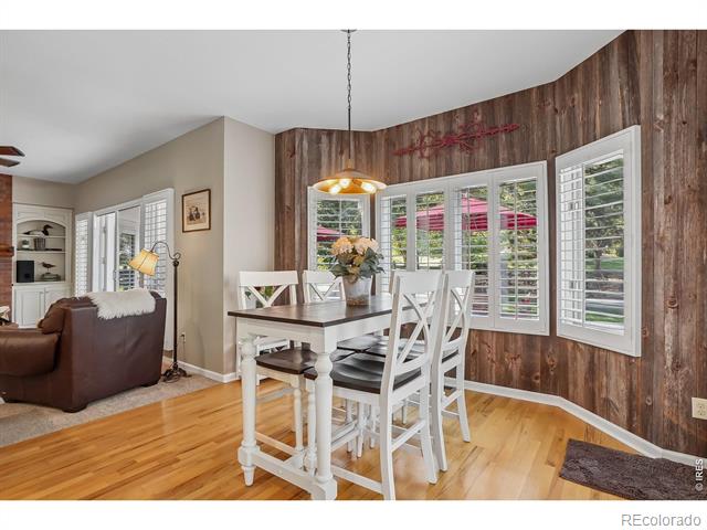 Dining area with white table and chairs, hardwood floors, and a wood-paneled wall with shuttered windows.