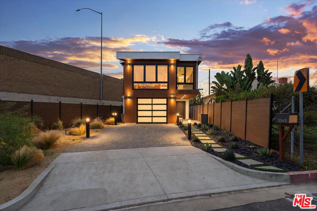 Modern two-story home with a wood-toned facade and landscaped driveway at dusk.