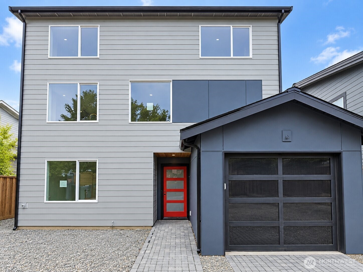 Modern gray two-story house with a red front door and dark glass-panel garage door.