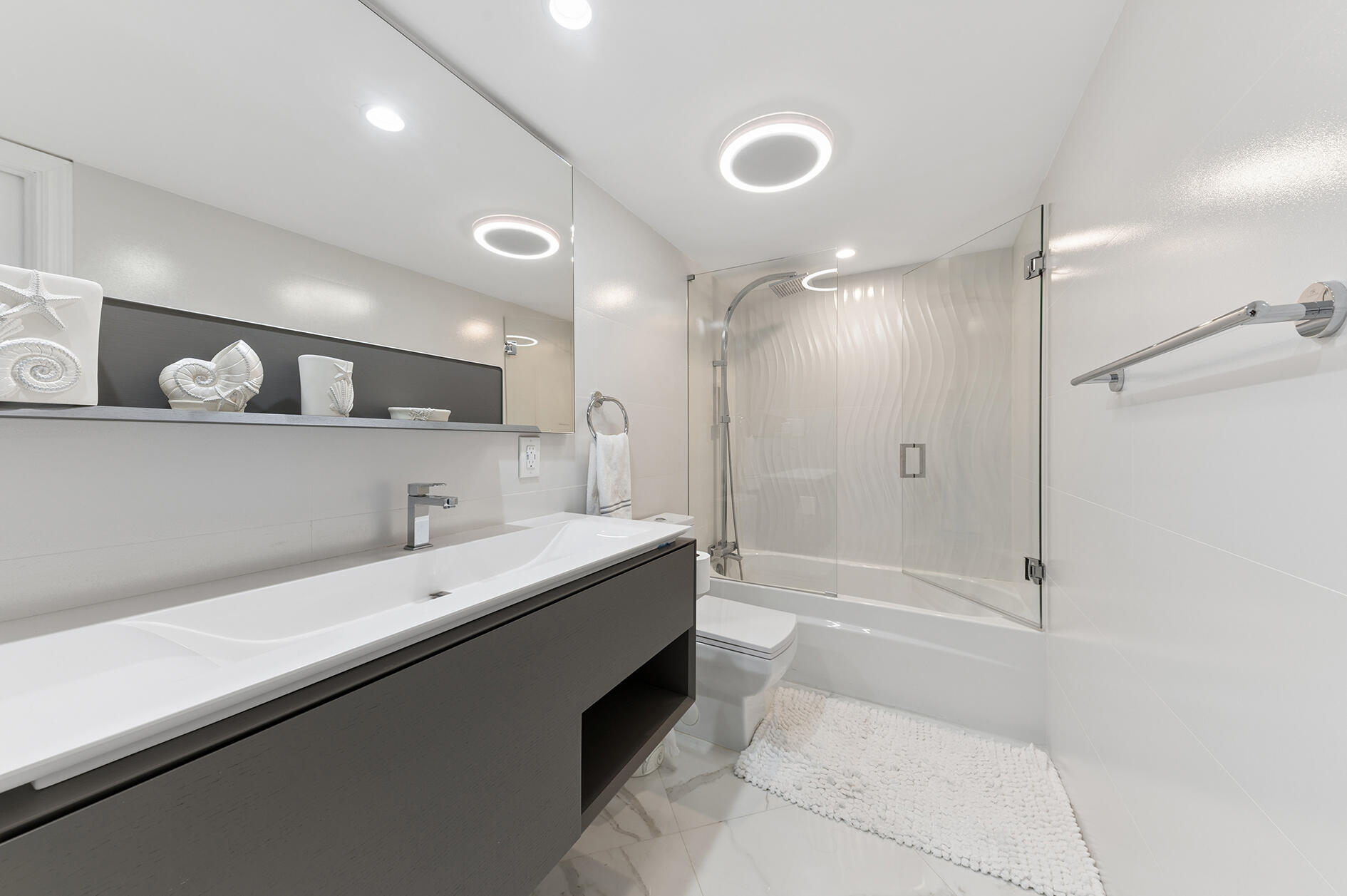 Modern bathroom with a dark floating vanity, sculptural seashell decor, and glass-enclosed tub and shower.