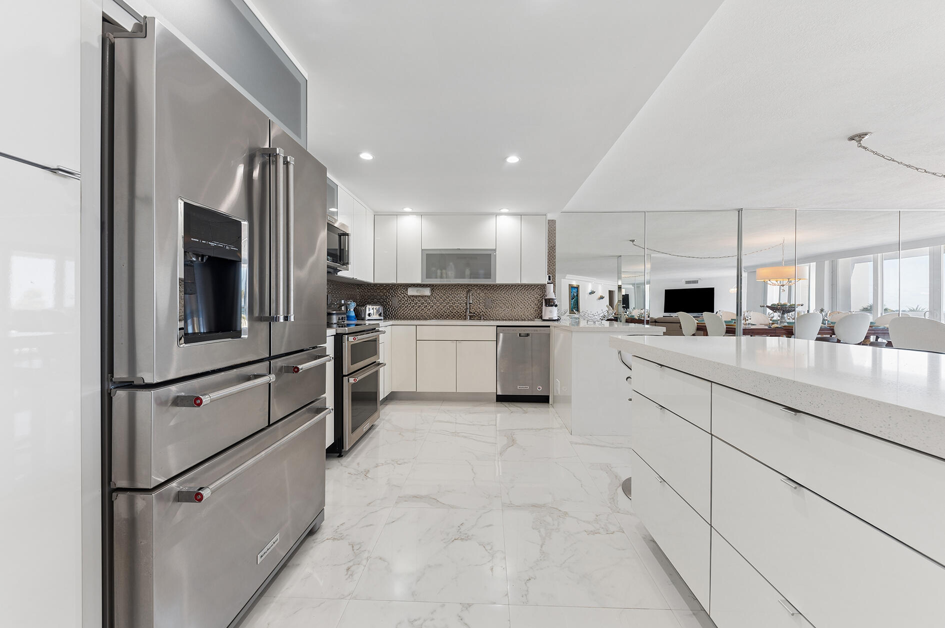 Modern kitchen with stainless steel appliances, white cabinetry, and a long island opening to the dining area.