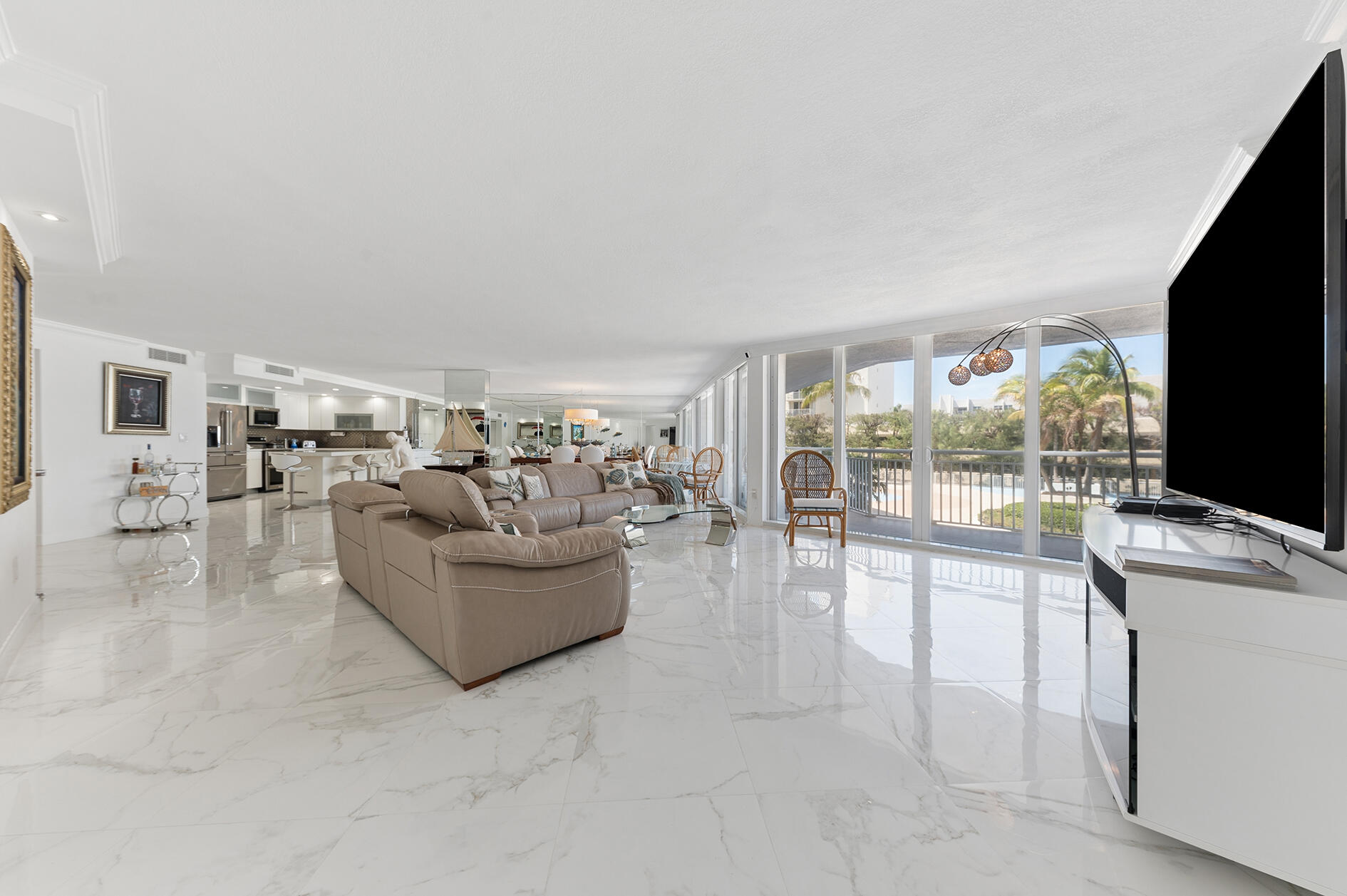 Open-plan living room with a sectional sofa, marble floors, and sliding doors to a balcony.