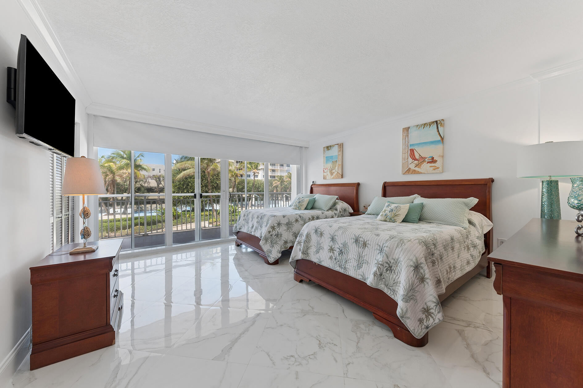 Bedroom with two beds, marble-look tile floors, and sliding doors opening to a balcony overlooking palms and a pool.