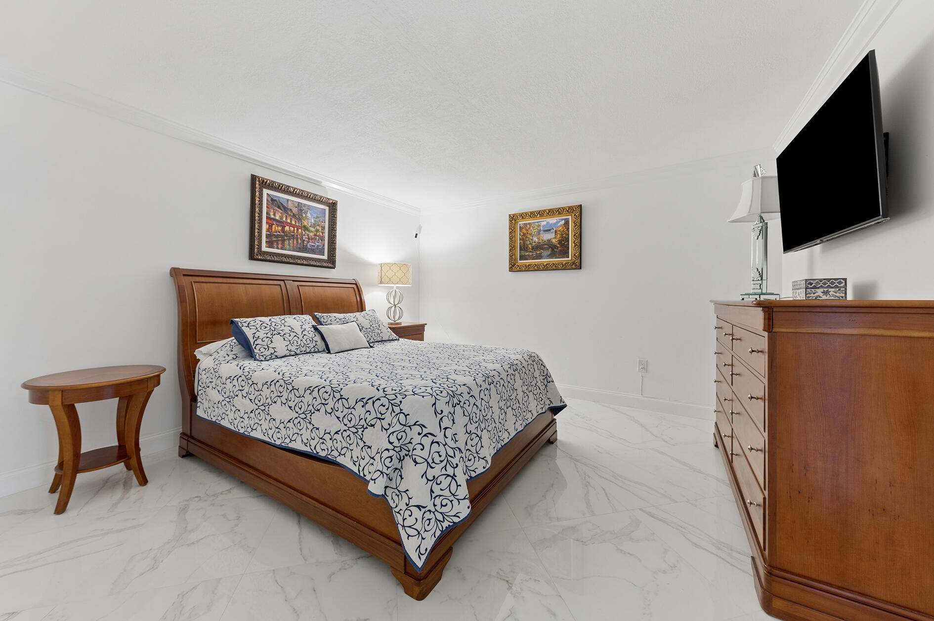 Bedroom with a wood bed, blue-and-white patterned bedding, marble floors, and a wall-mounted television.
