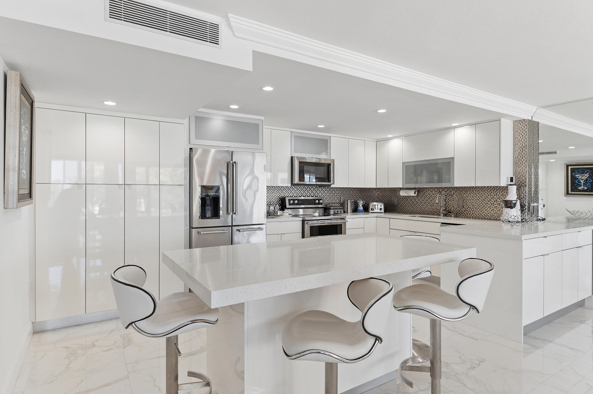 Modern white kitchen with a large island, stainless steel appliances, and bar stools.