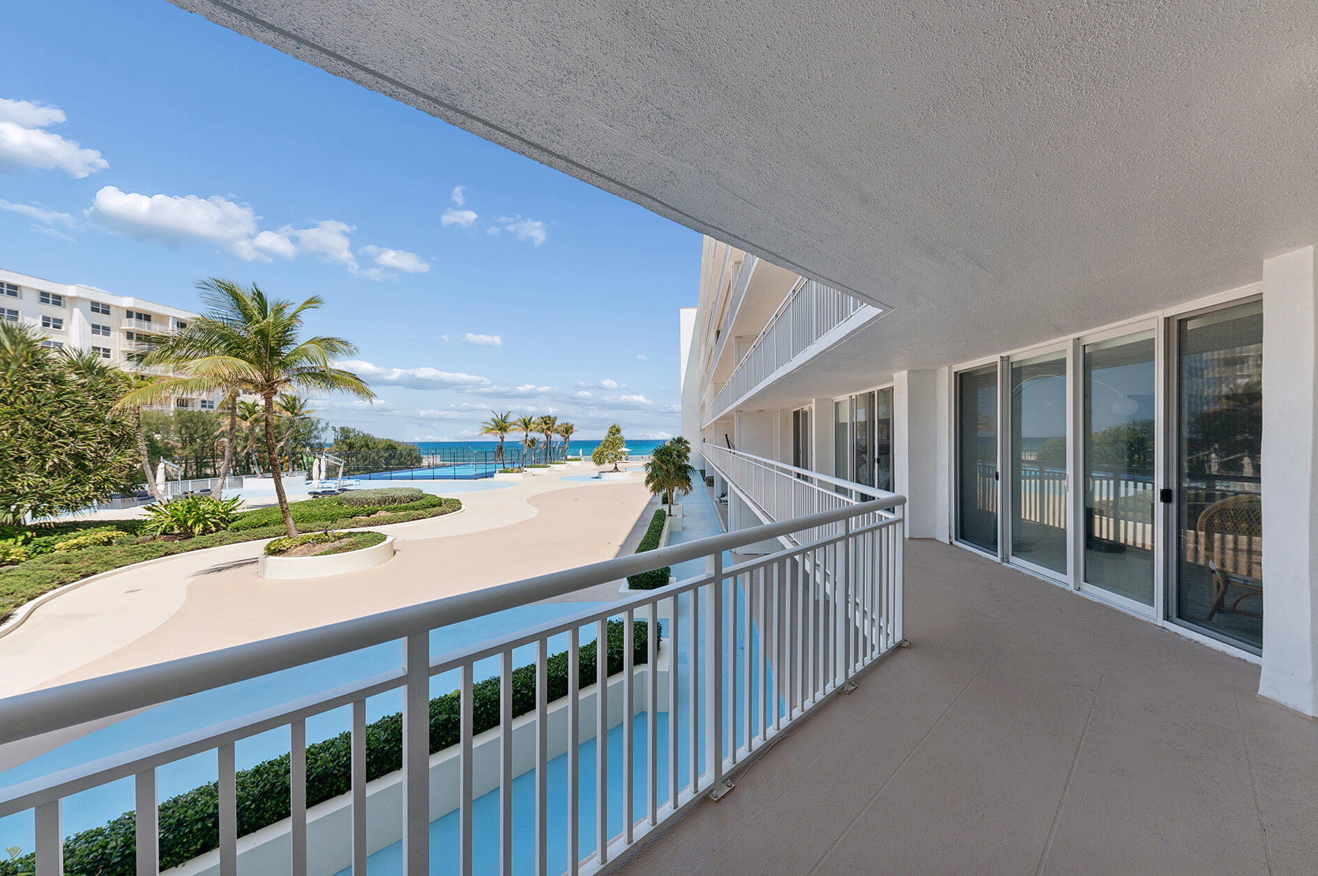 Condominium balcony overlooking a pool, palm trees, and the ocean.