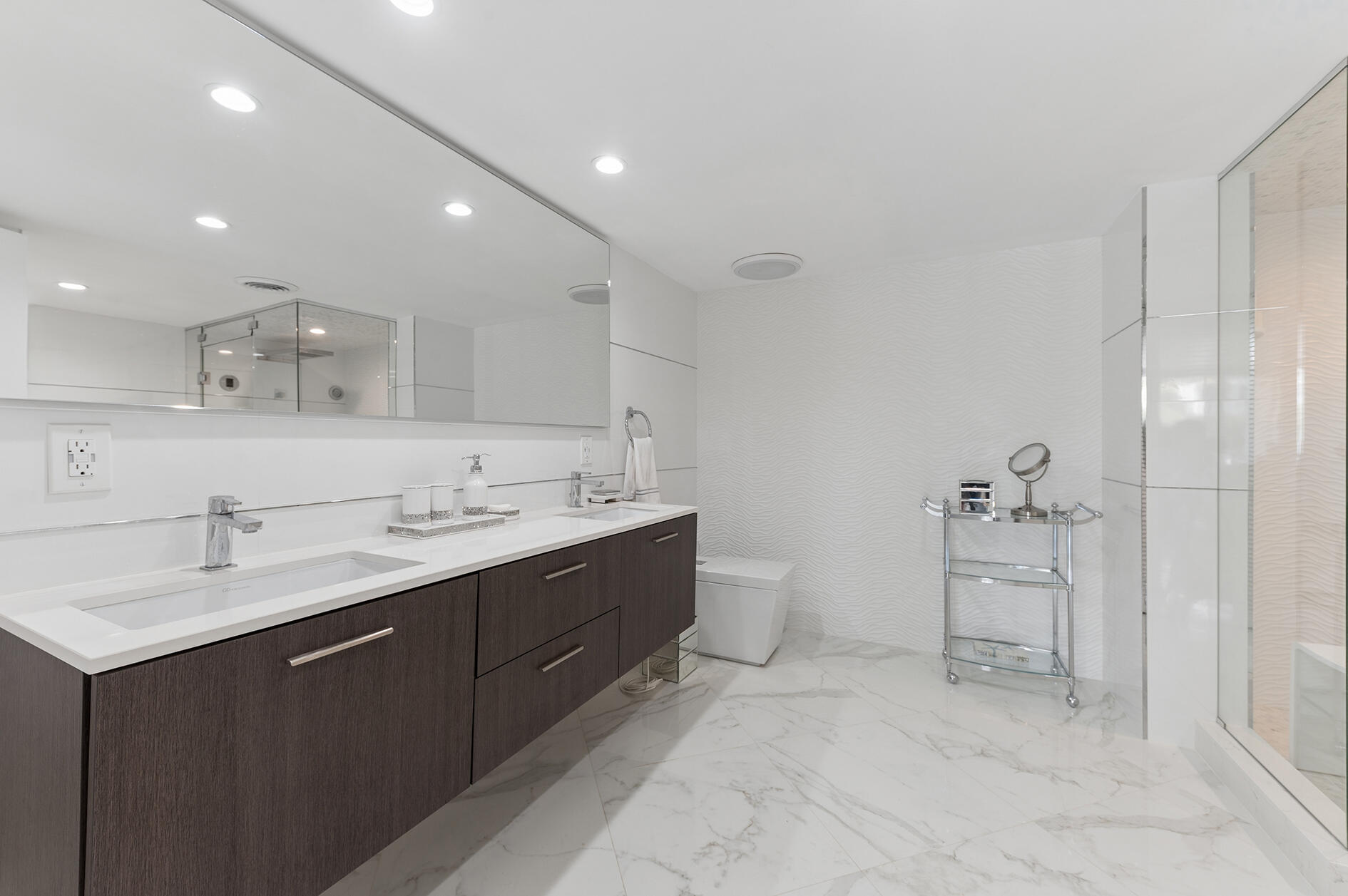 Modern bathroom with a double vanity, marble flooring, and a glass-enclosed shower.