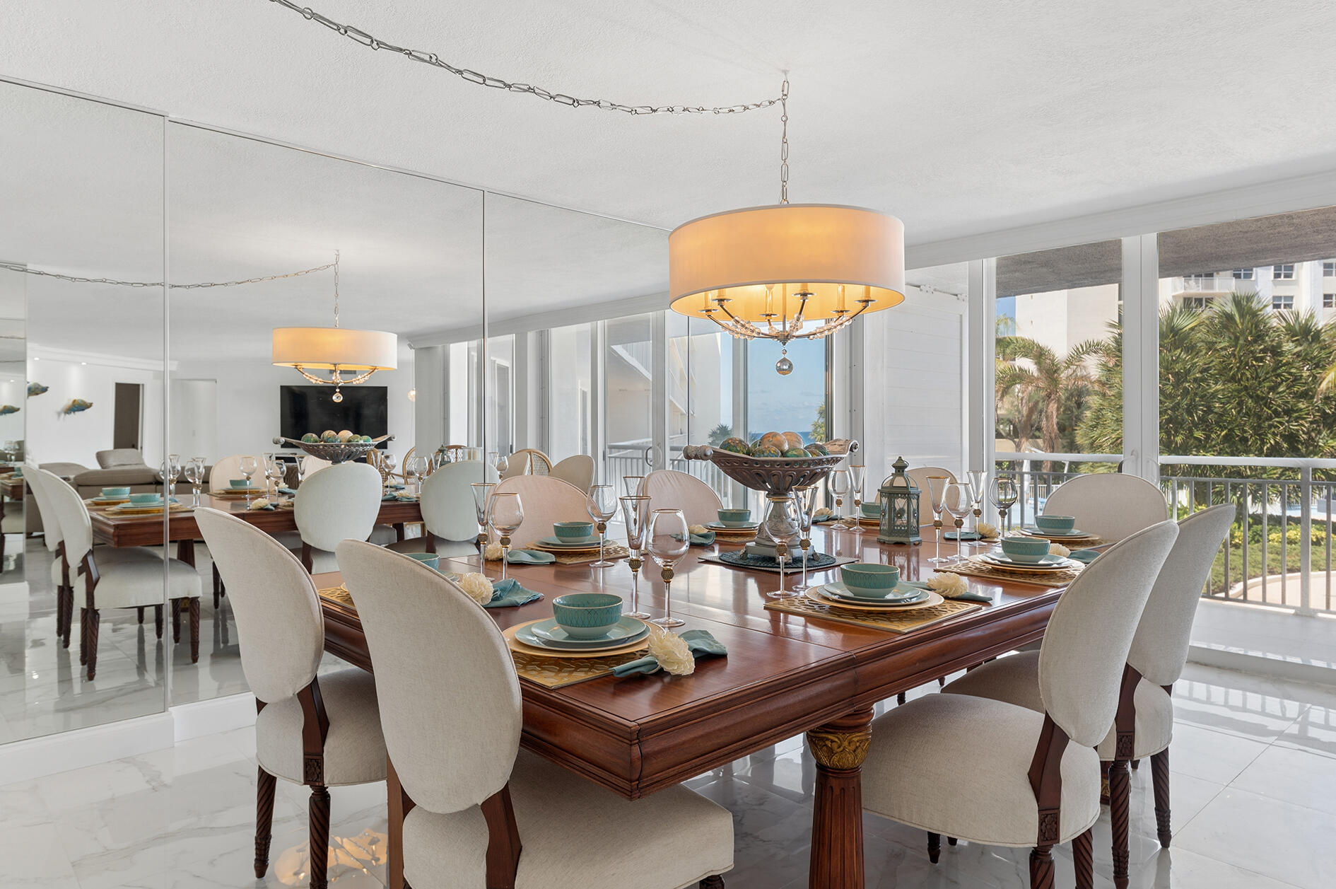 Dining room with a formal set table, mirrored wall, and windows overlooking palm trees.
