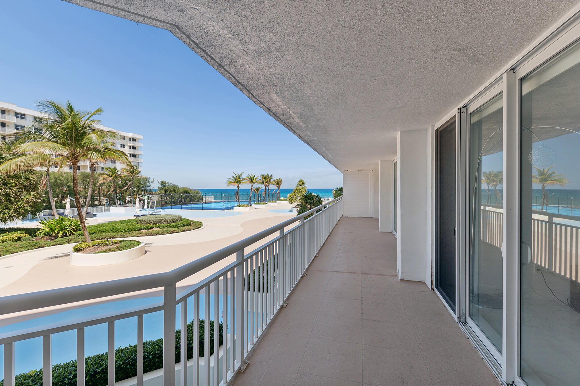 Covered condo balcony overlooking an oceanfront pool, palm trees, and the Atlantic Ocean.