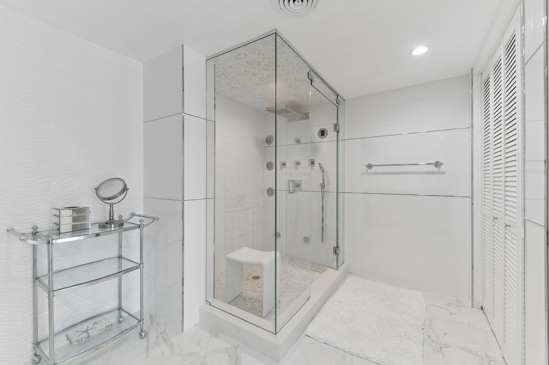 White bathroom with a glass-enclosed shower, wave-textured tile, and marble flooring.