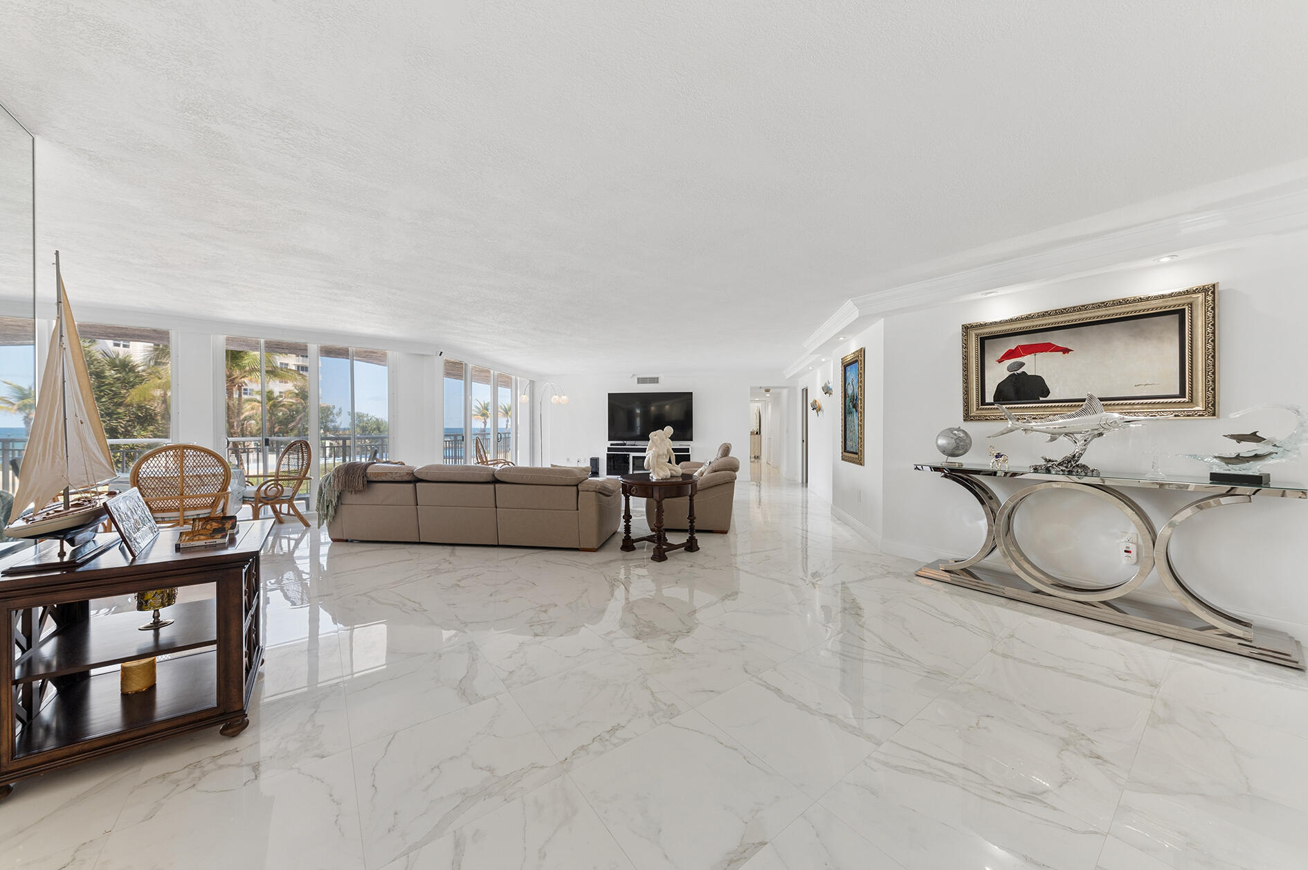 Bright living room with floor-to-ceiling windows overlooking the ocean and glossy marble floors.
