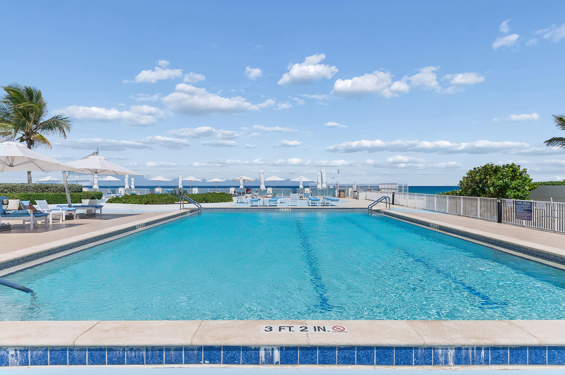 Outdoor swimming pool overlooking the ocean, with lounge chairs and white umbrellas.