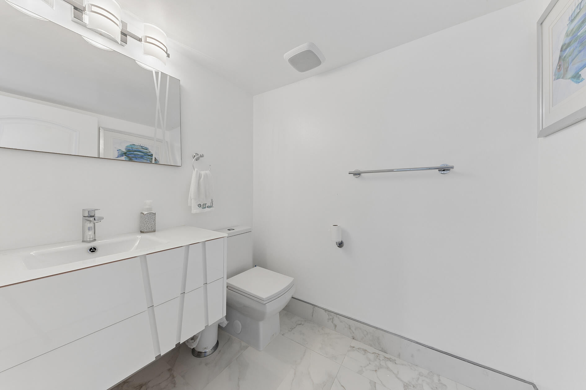 Bright white bathroom with a modern vanity, toilet, and marble-look tile flooring.