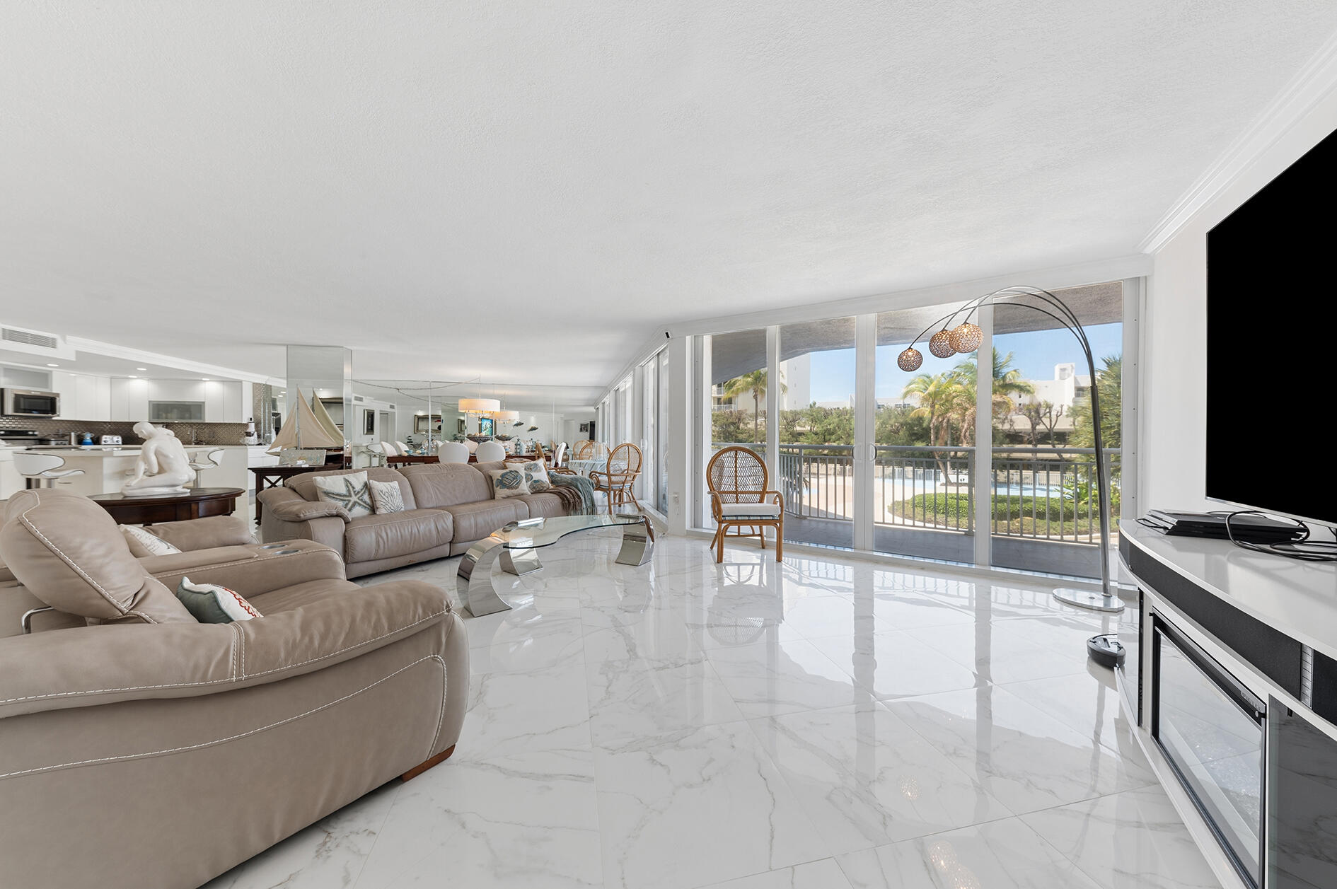 Open-plan living room with marble floors, a glass balcony, and poolside views.
