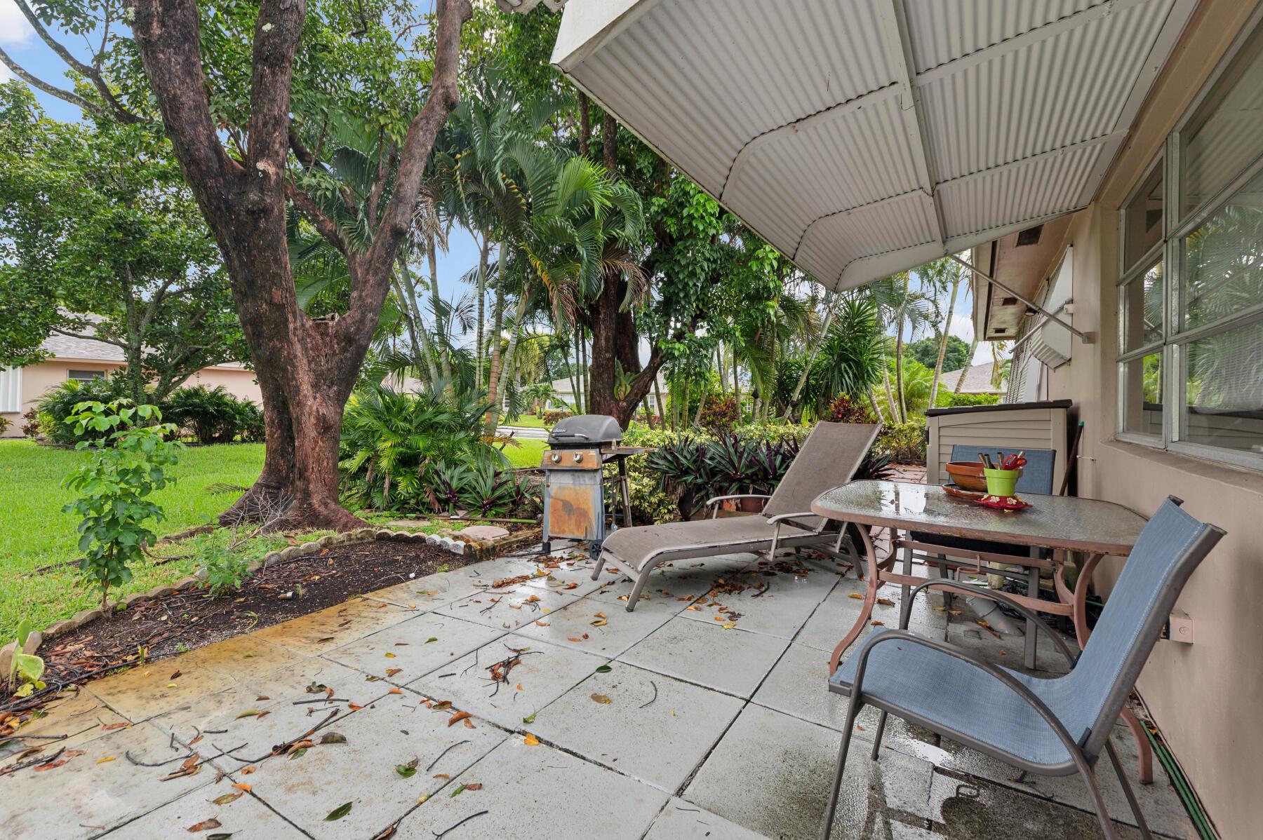 Covered patio with outdoor dining furniture, a barbecue grill, and lush tropical landscaping.