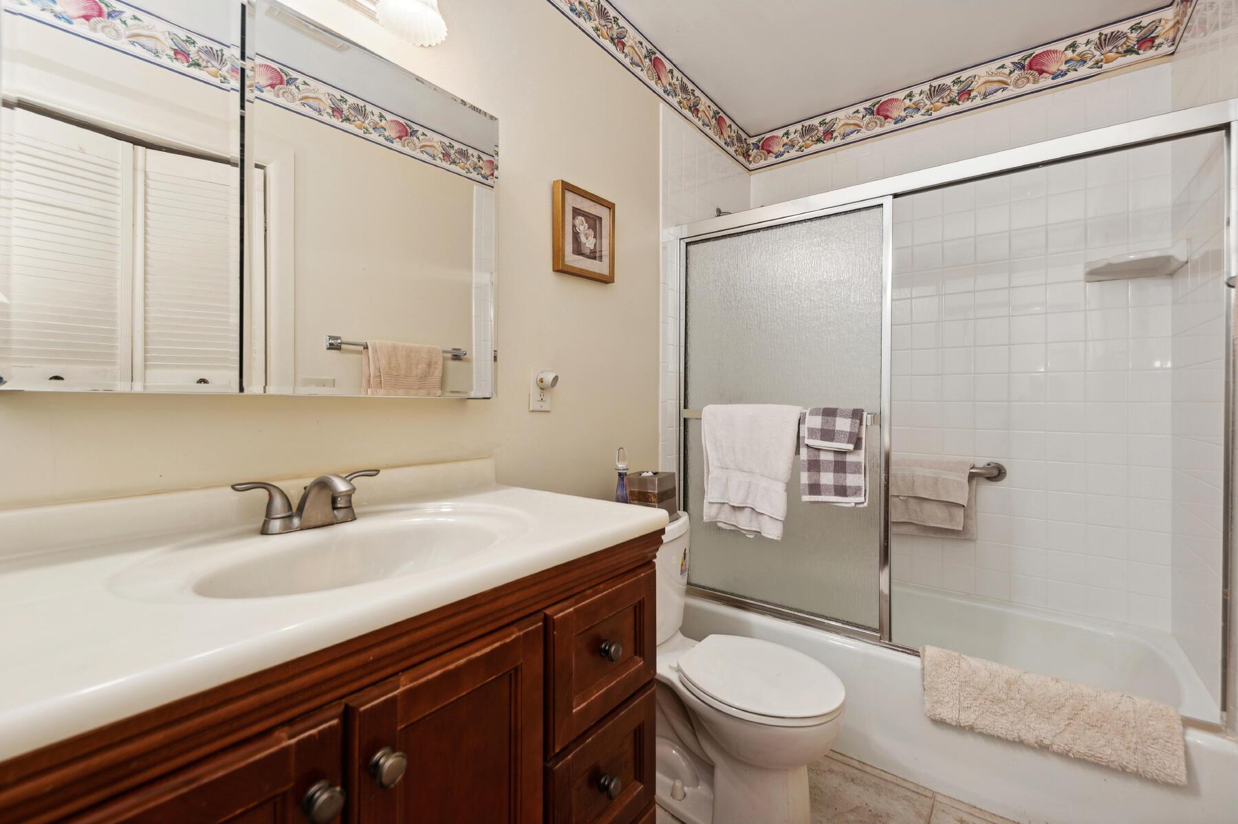 Bathroom with a dark wood vanity, white tiled tub and shower, and colorful seashell border trim.