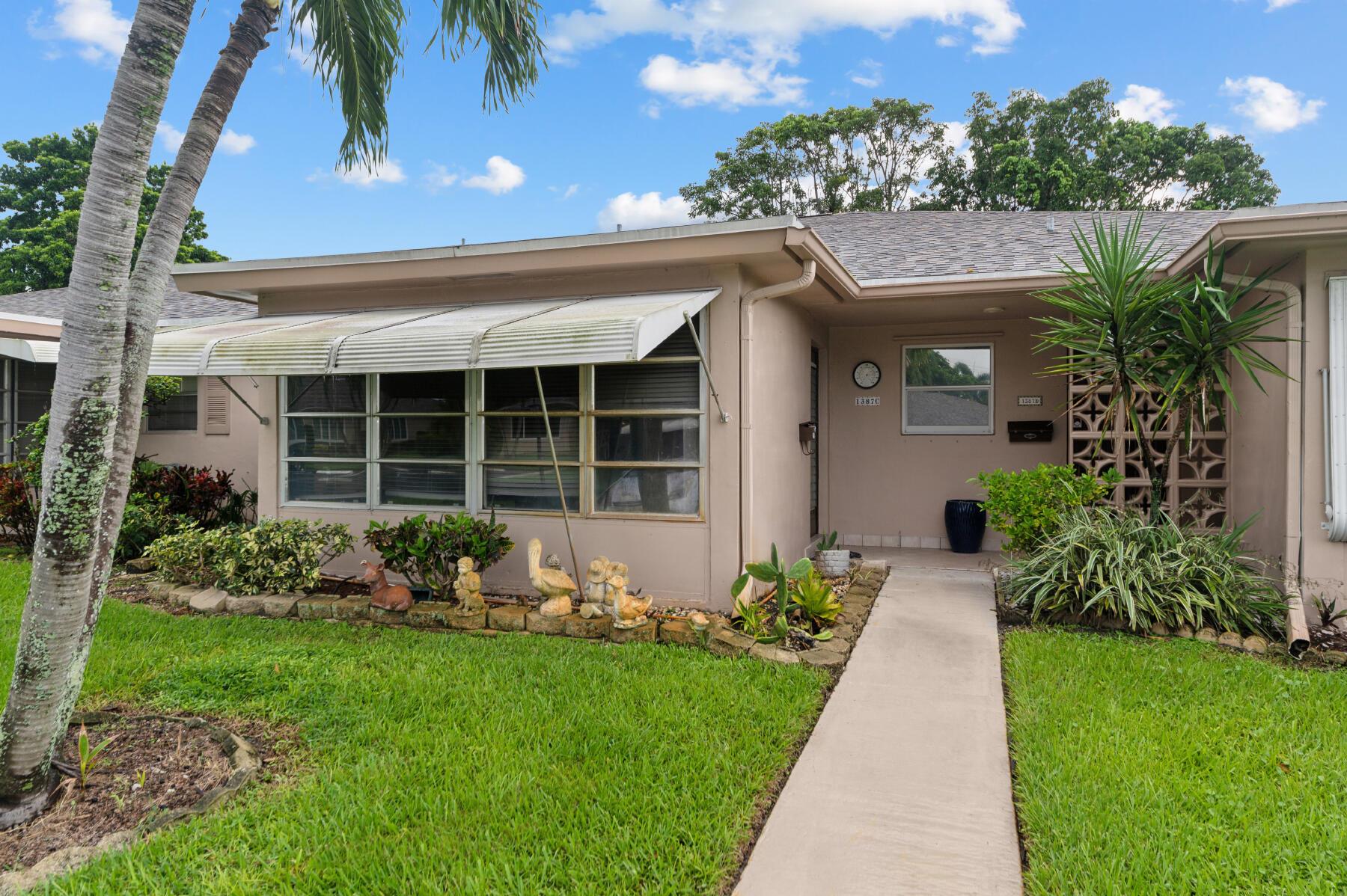 Single-story home with a broad window awning, covered entry, palm trees, and a landscaped front yard.