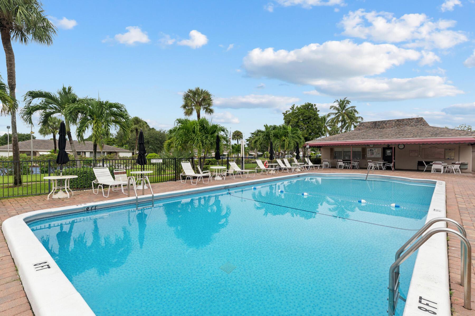 Community swimming pool with palm trees, lounge chairs, and a clubhouse.