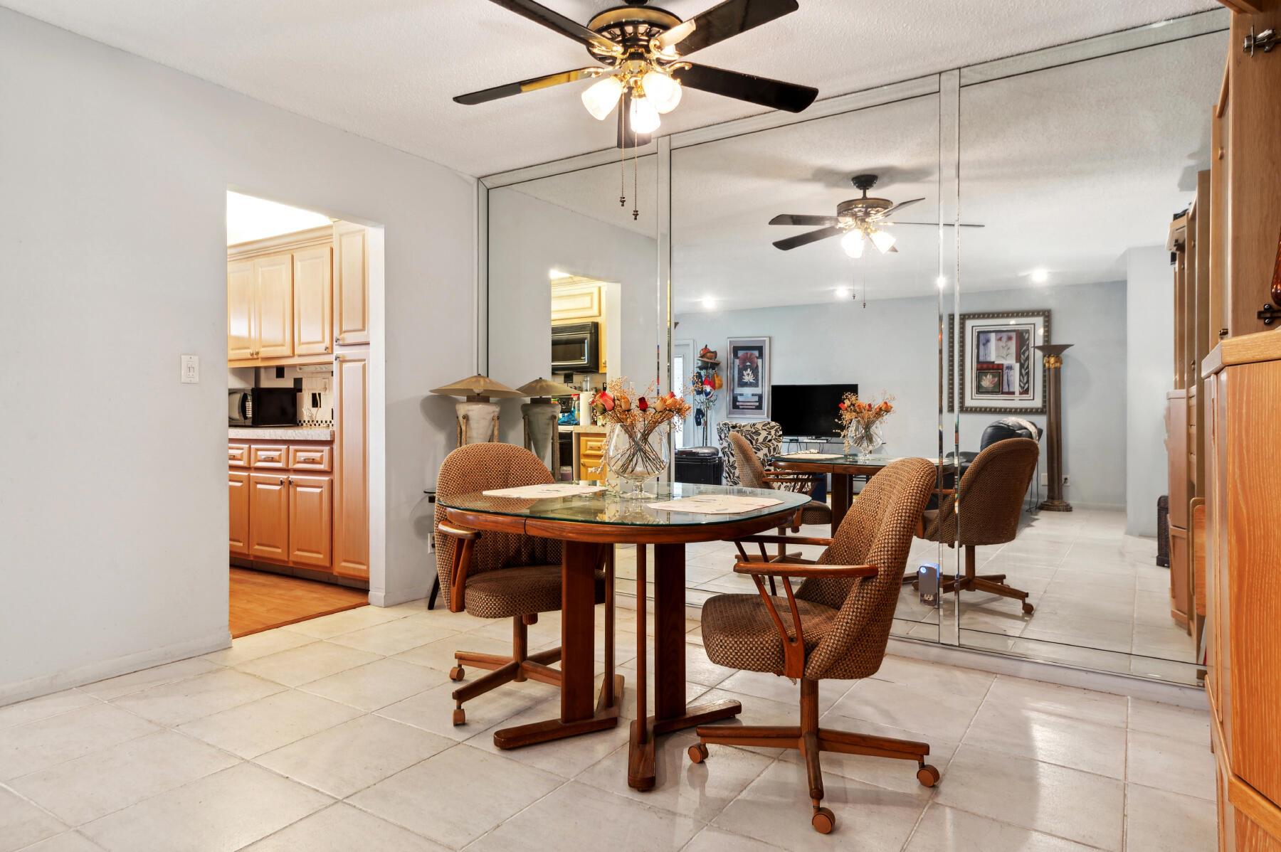 Dining area with a glass-top table, rolling chairs, and mirrored wall panels reflecting the living room.