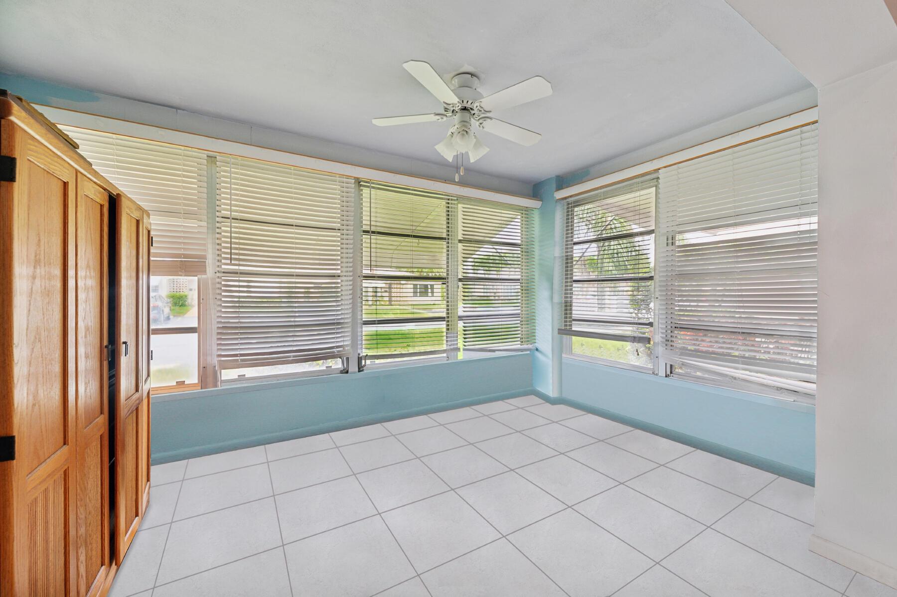 Vacant tiled sunroom with turquoise walls, wide blinded windows, and a tall wooden cabinet.