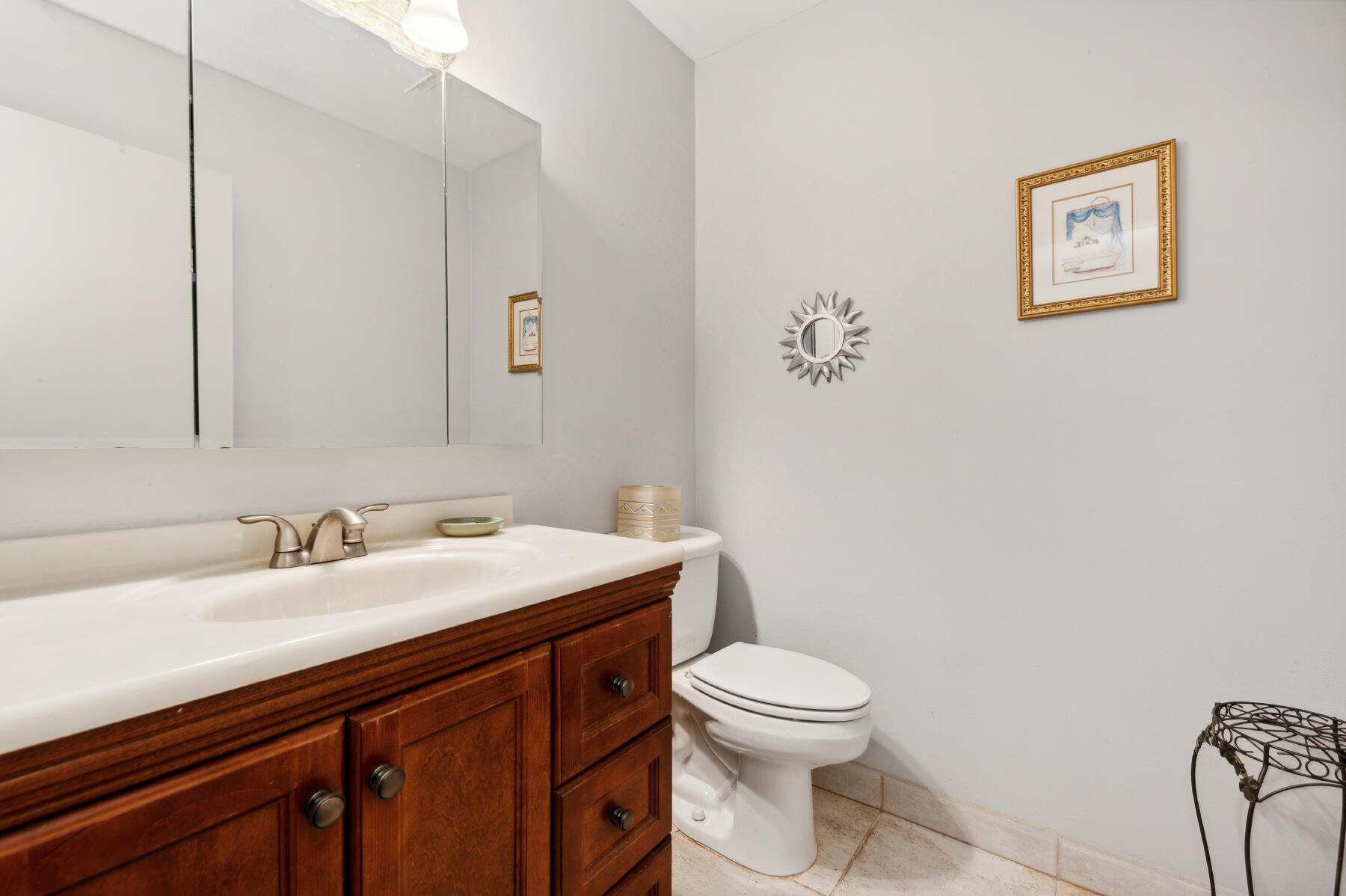 Bathroom with a dark wood vanity, large mirror, toilet, and decorative sunburst mirror.