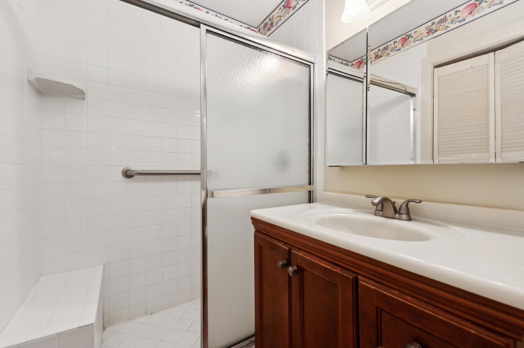 Bathroom with frosted-glass shower, tiled bench, and dark wood vanity beneath a mirrored cabinet.