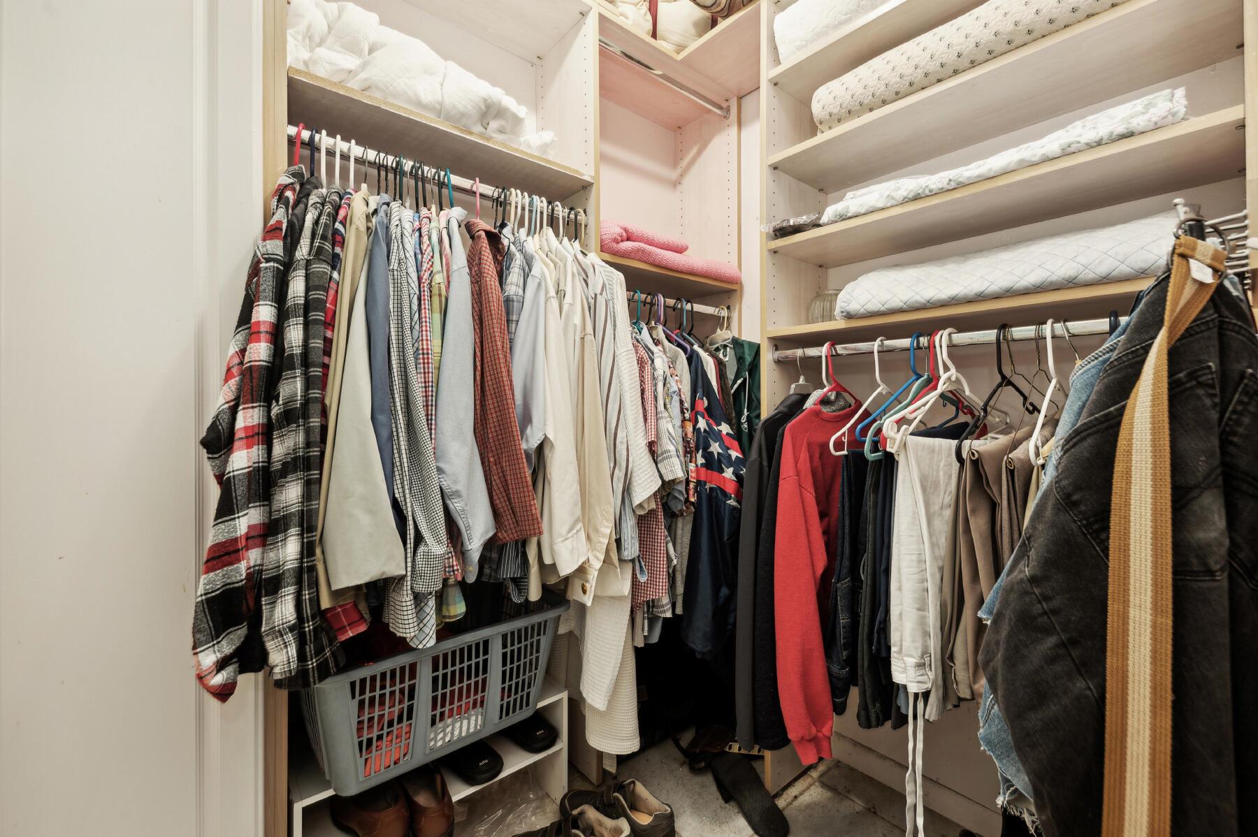 Walk-in closet with hanging clothes, folded linens on shelves, and a laundry basket.
