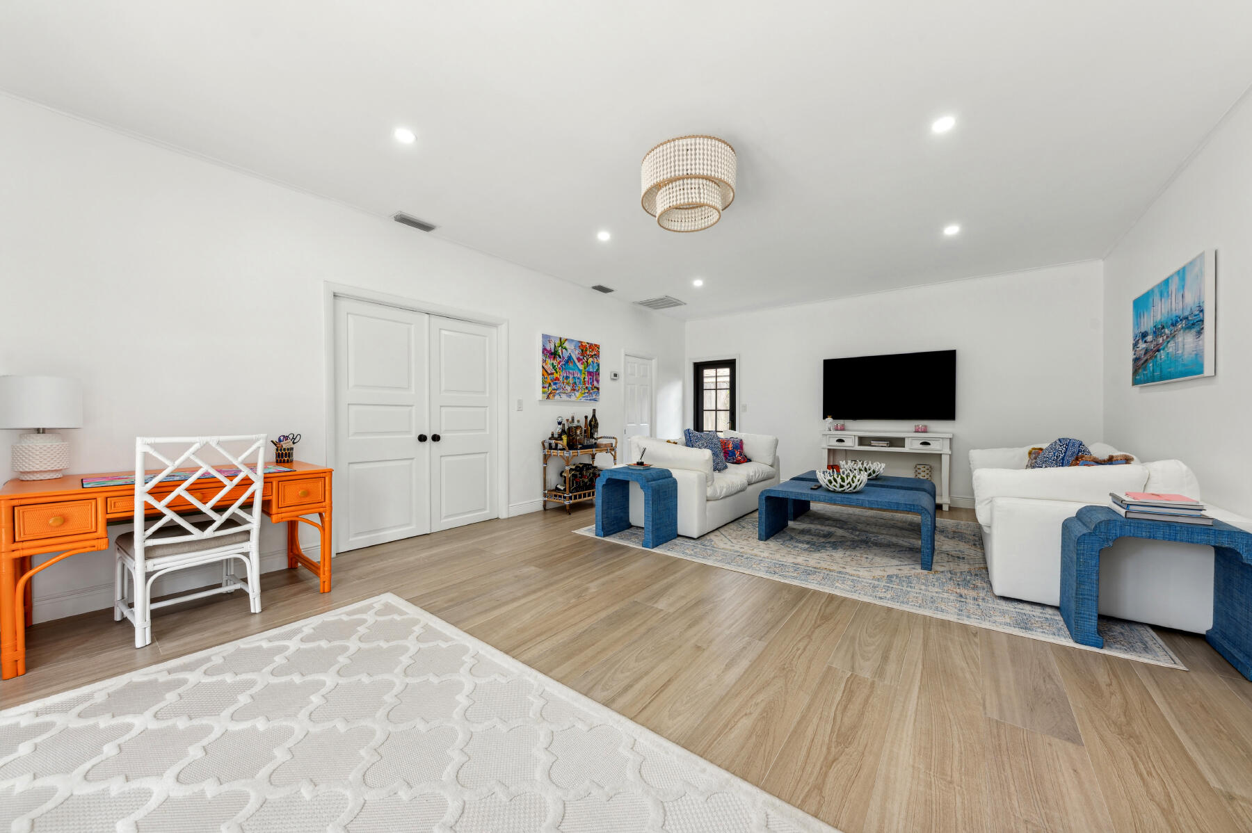 Living room with white sofas, blue coffee tables, and a vivid orange desk.
