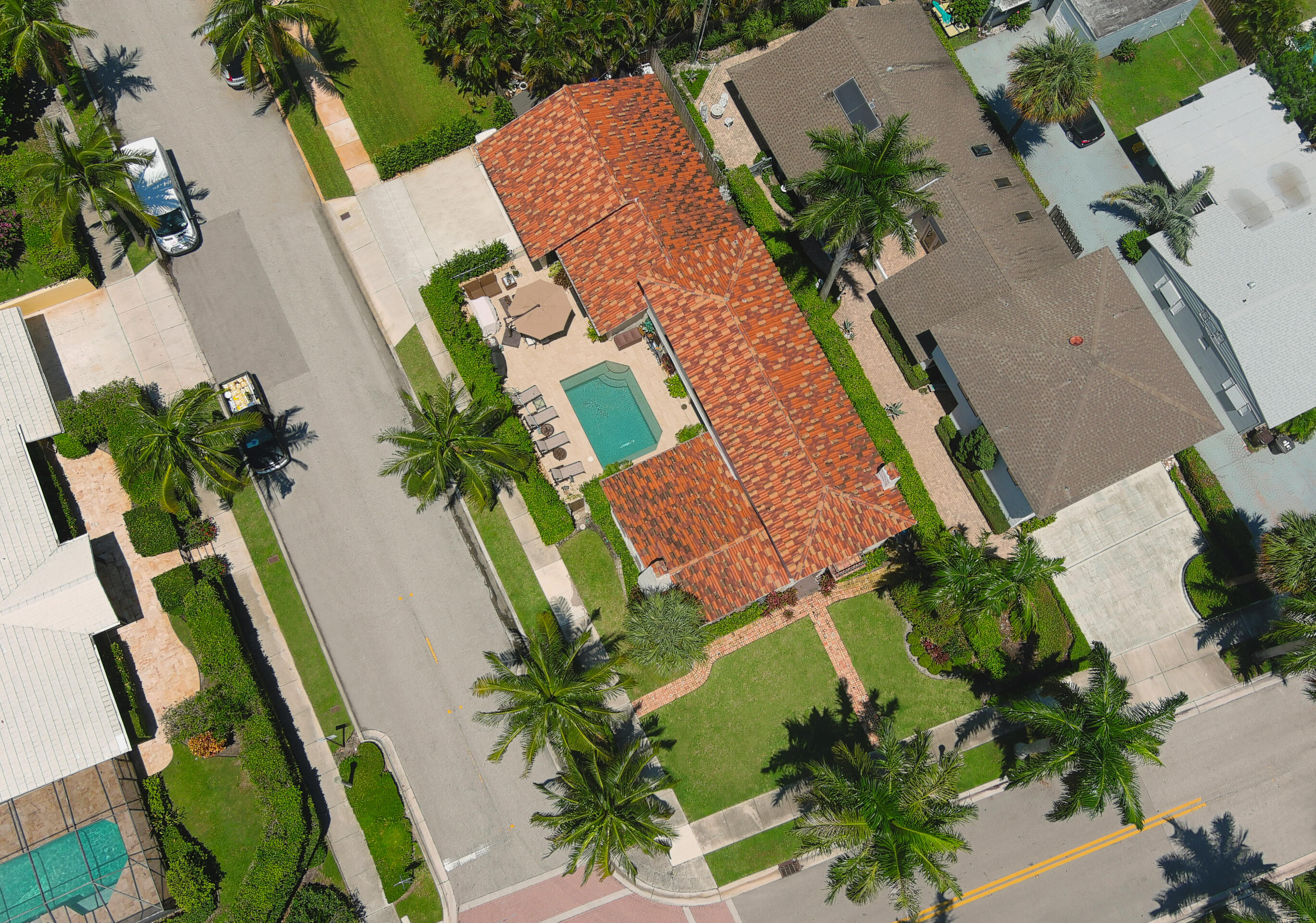 Aerial view of a red tile-roofed home with a backyard pool and palm-lined landscaping.