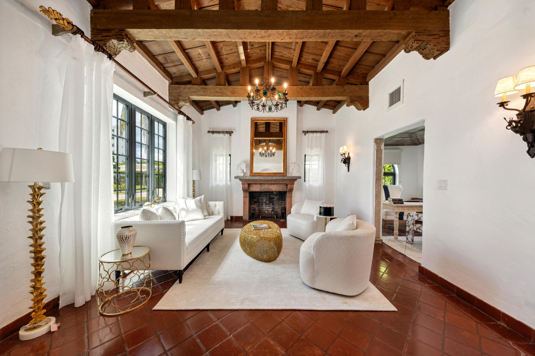 Living room with exposed timber beams, a fireplace, white seating, and terracotta tile floors.