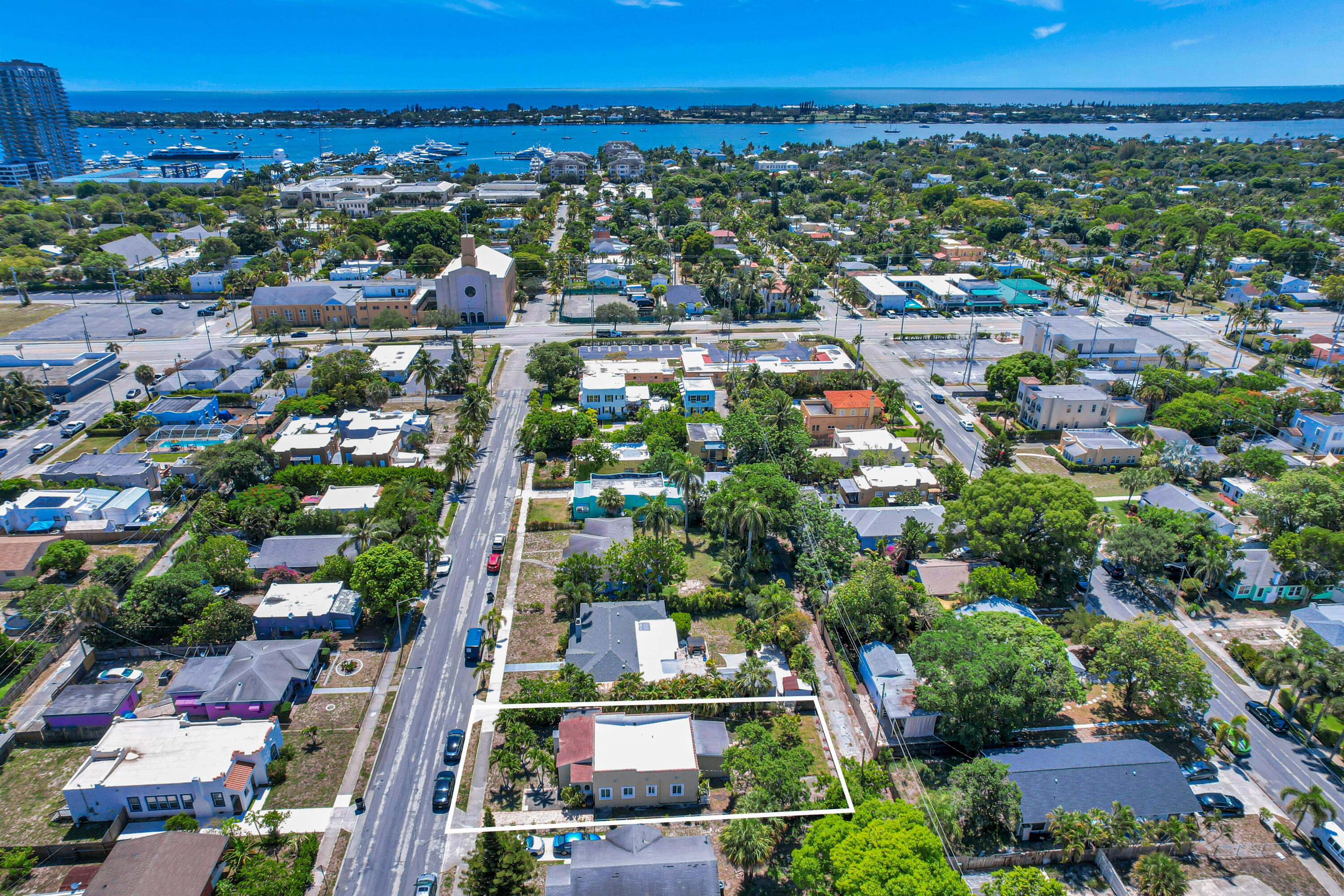 Aerial view of the outlined property in a leafy neighborhood, with boats on the waterway in the distance.