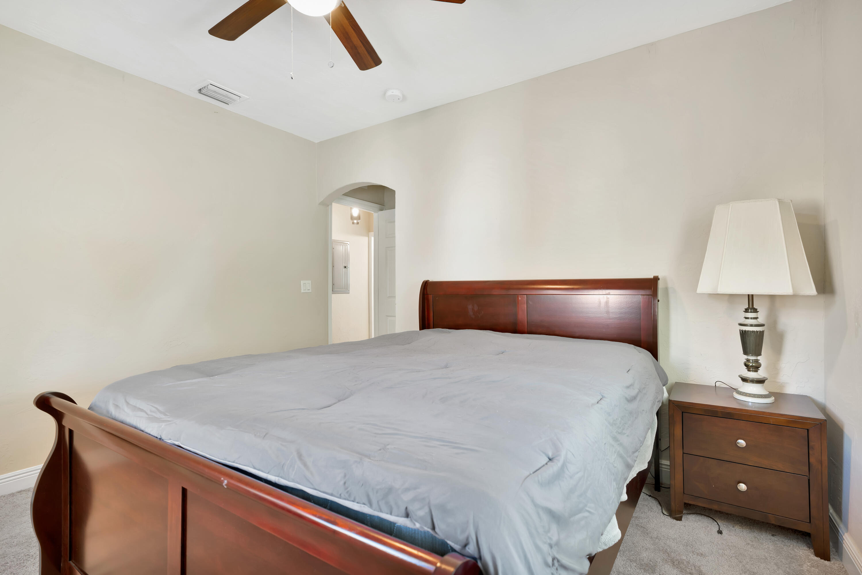 Bedroom with a dark wood bed frame, gray bedding, and matching nightstand with lamp.