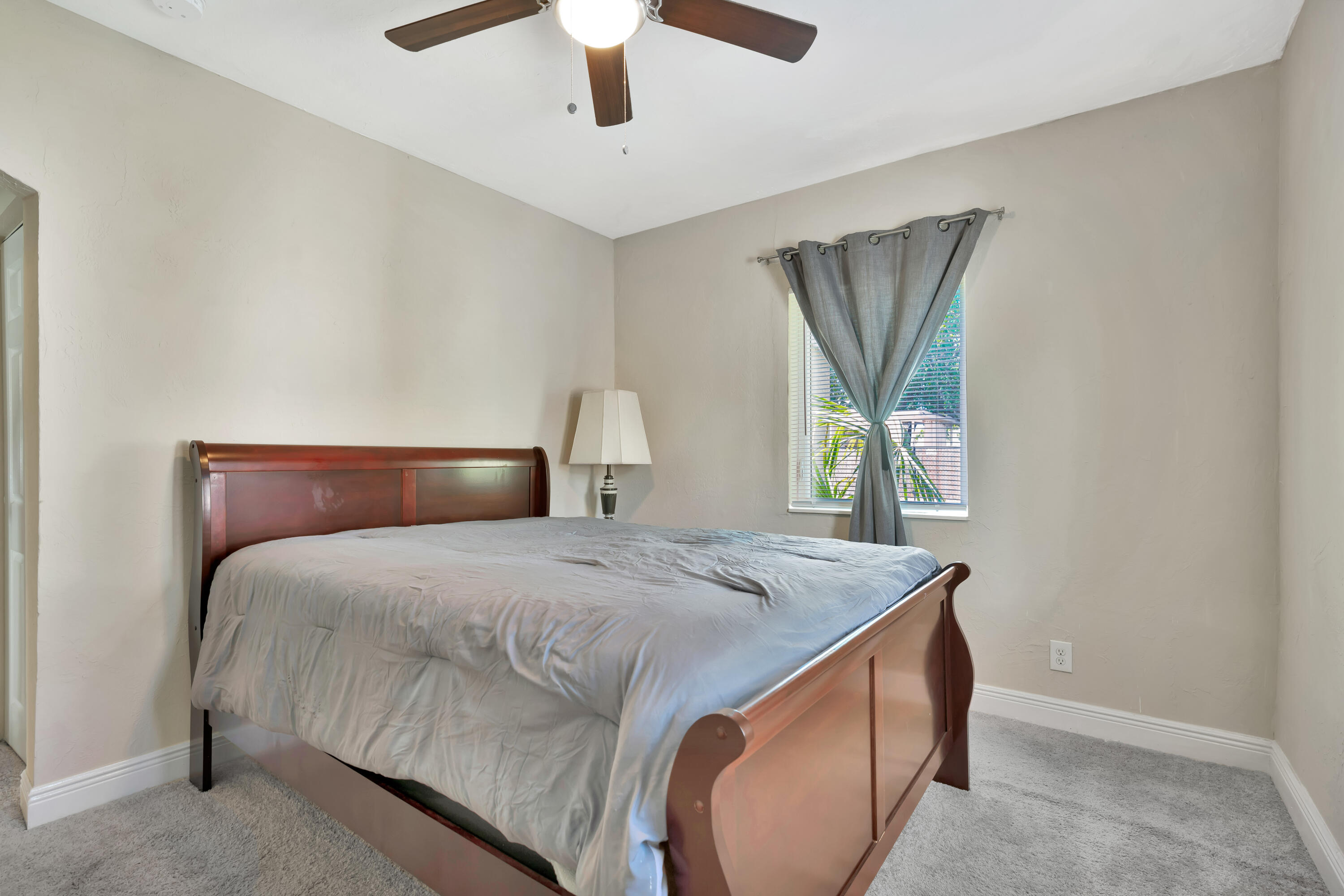 Bedroom with a dark wood bed and gray bedding beside a curtained window.