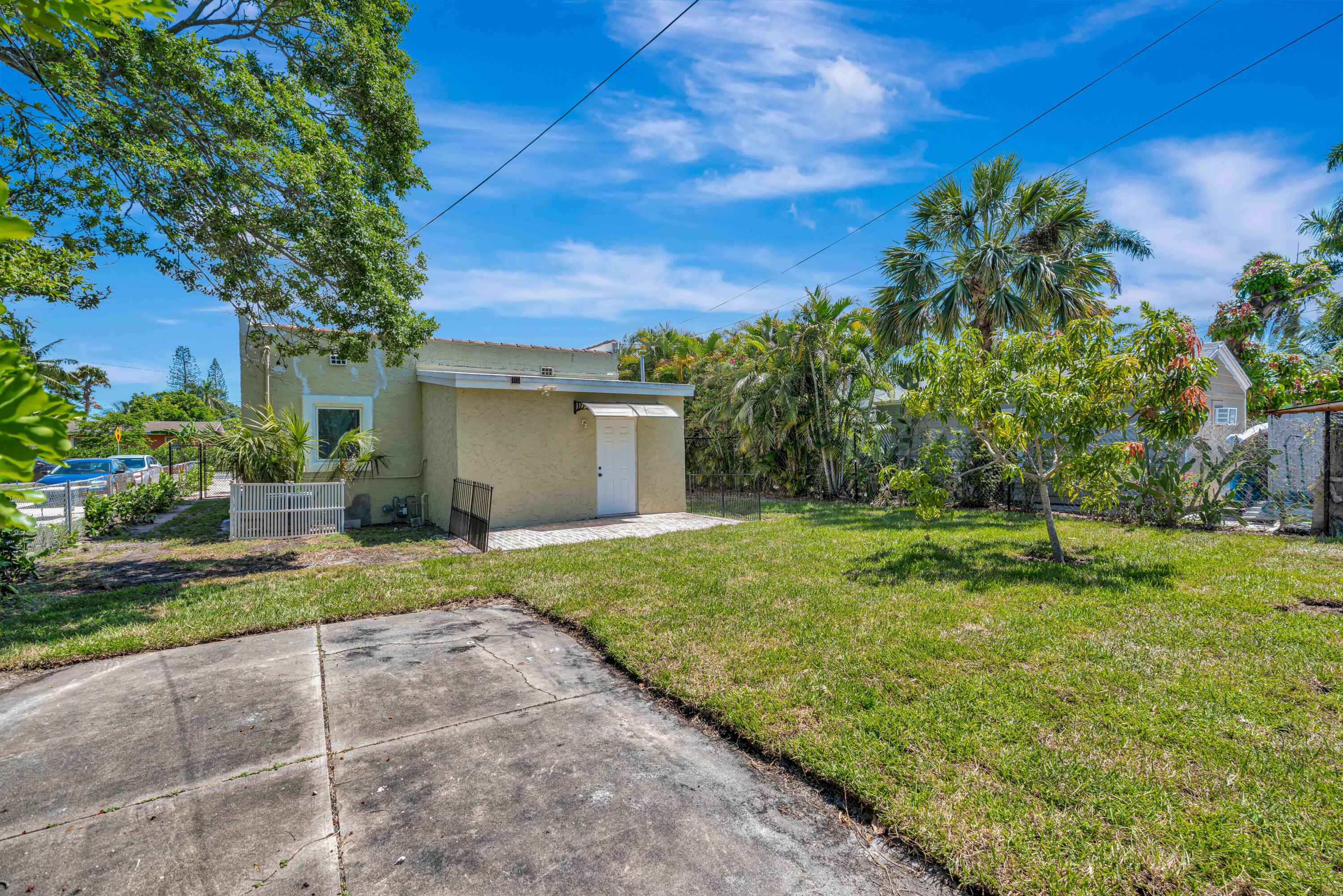 Beige stucco building beside a grassy yard with palm trees and a concrete driveway.
