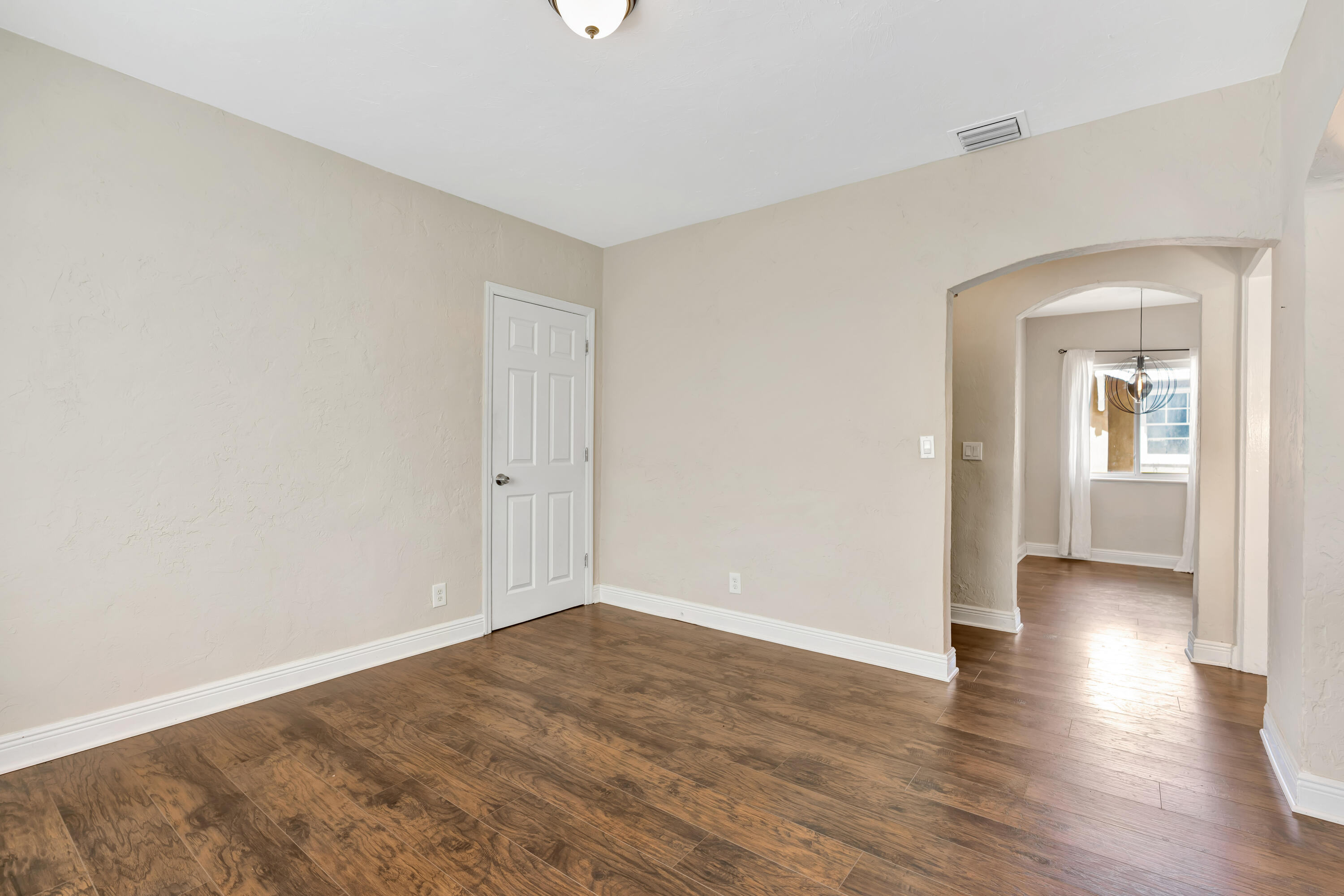 Empty room with wood-look flooring and an arched opening to a bright room with a window.