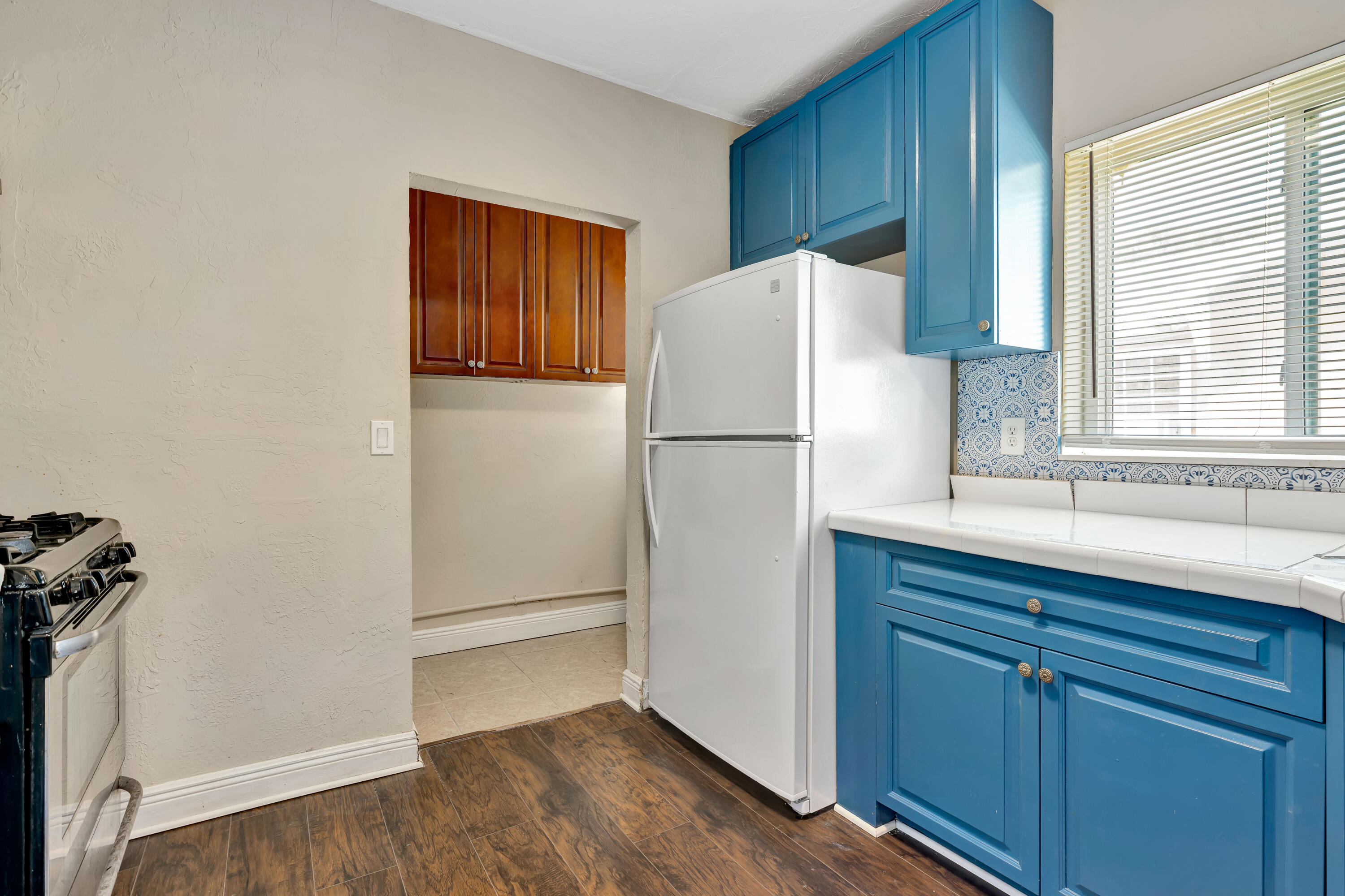 Kitchen with bright blue cabinets, a white refrigerator, patterned backsplash, and a window with blinds.