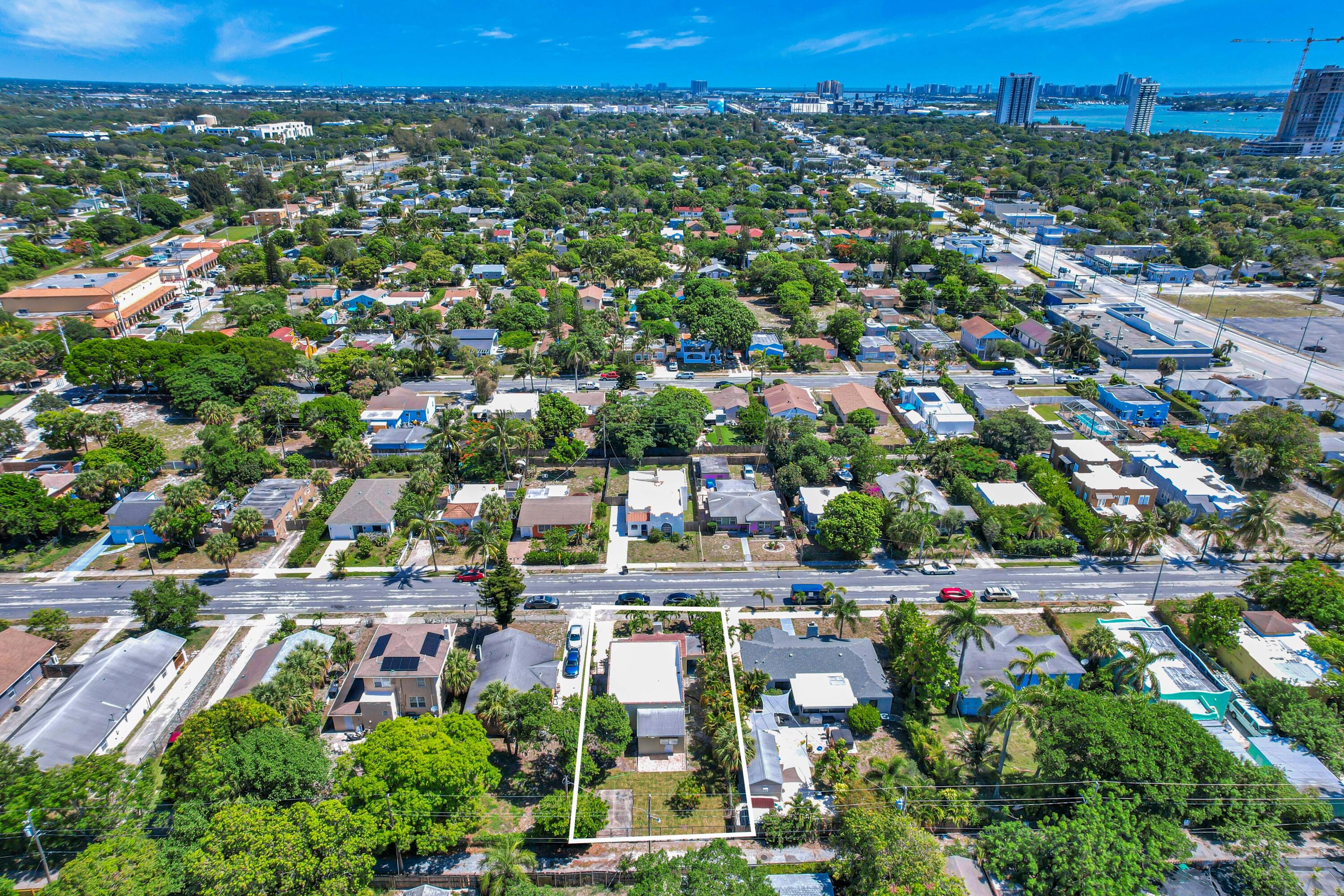 Aerial view of a white-outlined property lot amid palm-lined homes, with the skyline and water in the distance.