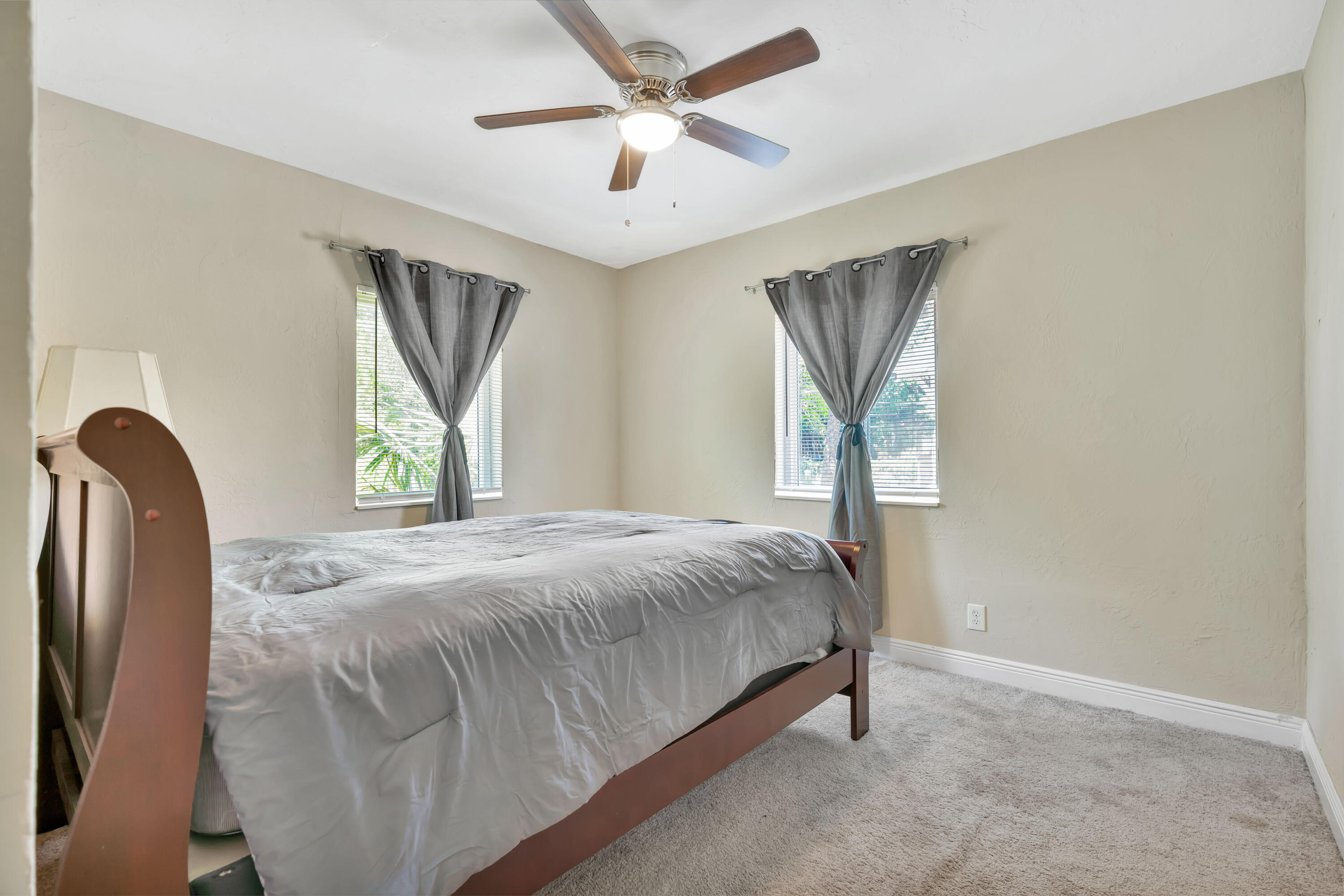 Bedroom with a large wooden bed, gray bedding, tied-back curtains, and a ceiling fan.