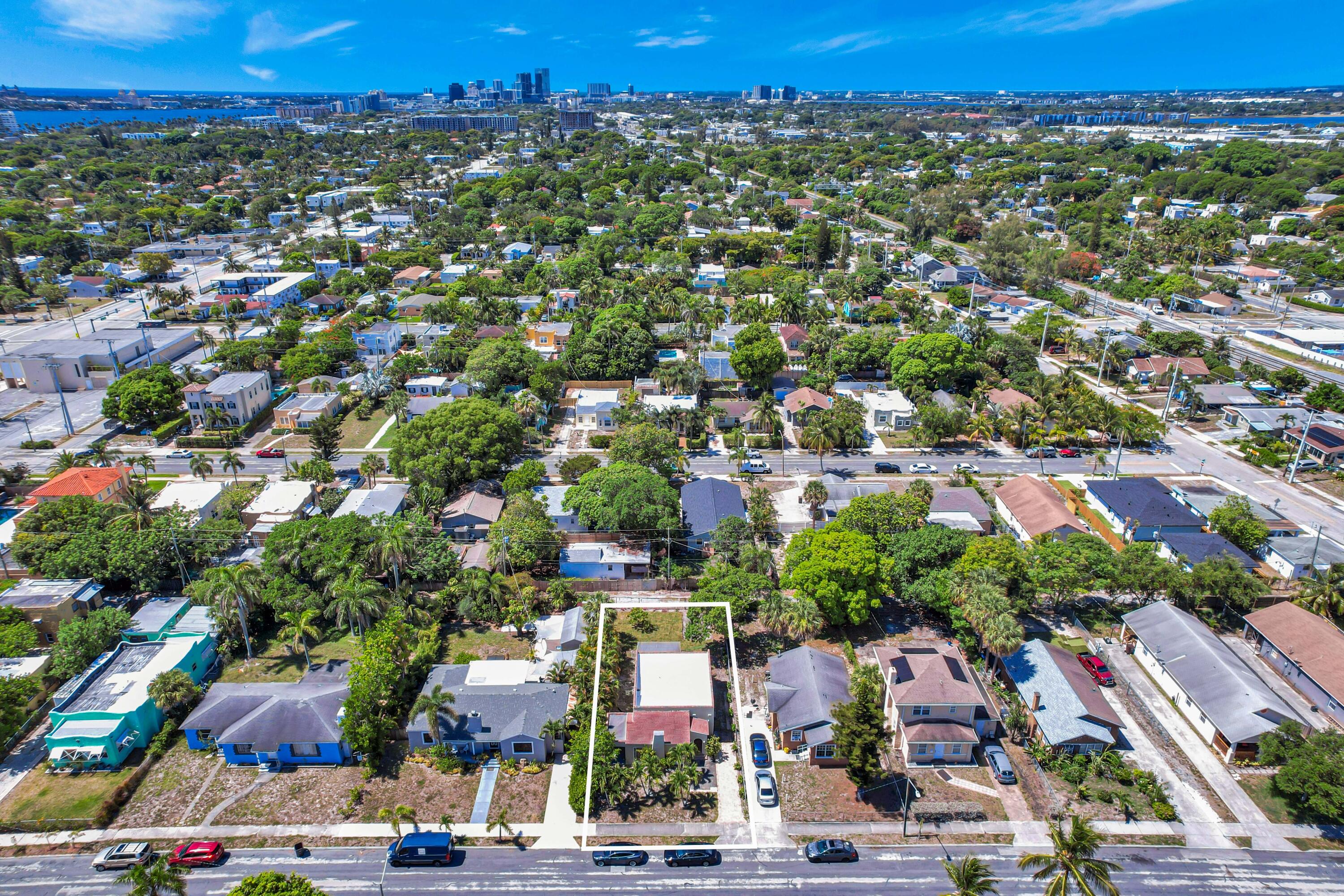 Aerial view of a marked residential parcel amid leafy homes, with a downtown skyline in the distance.