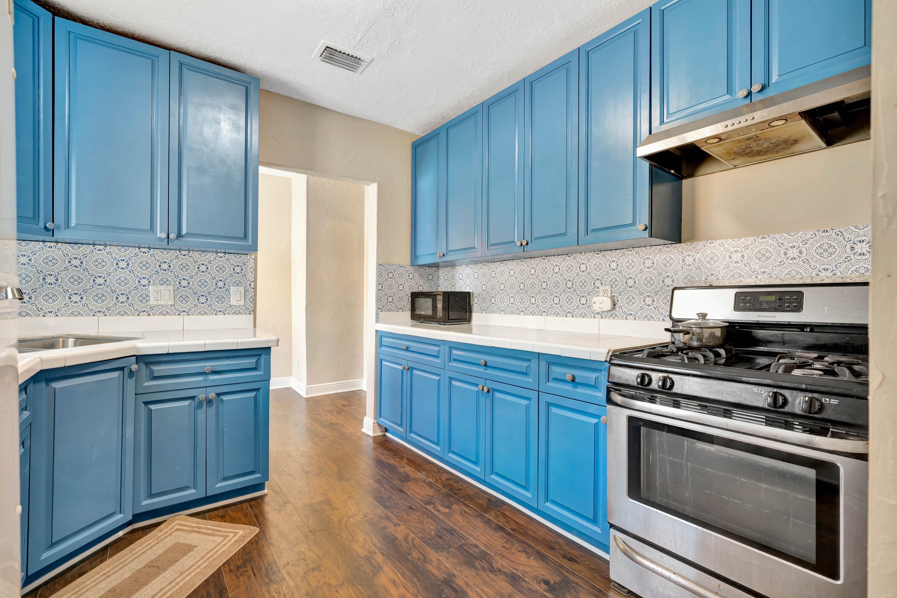 Kitchen with bright blue cabinets, patterned tile backsplash, and stainless-steel gas range.
