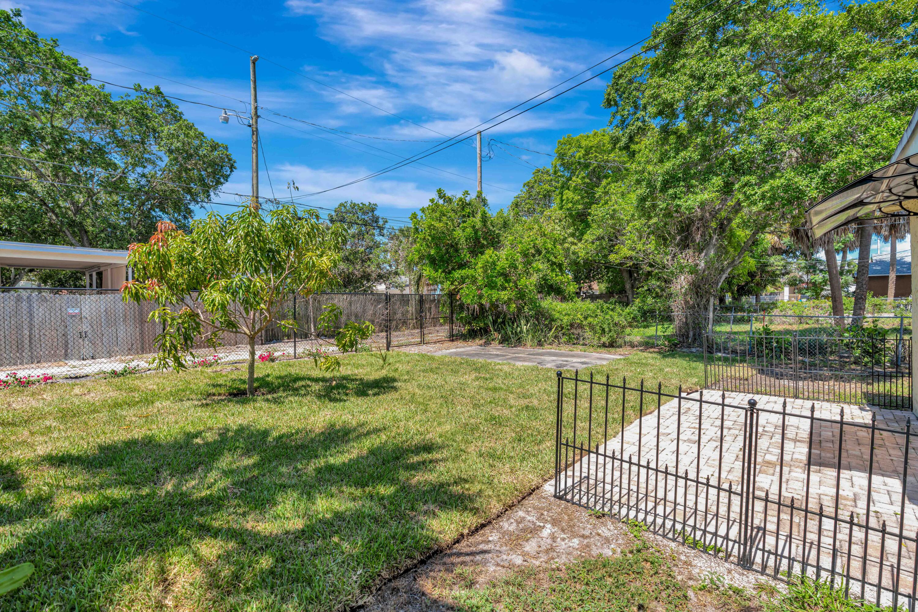 Fenced backyard with a broad lawn, leafy trees, and a paved patio enclosed by black metal railings.