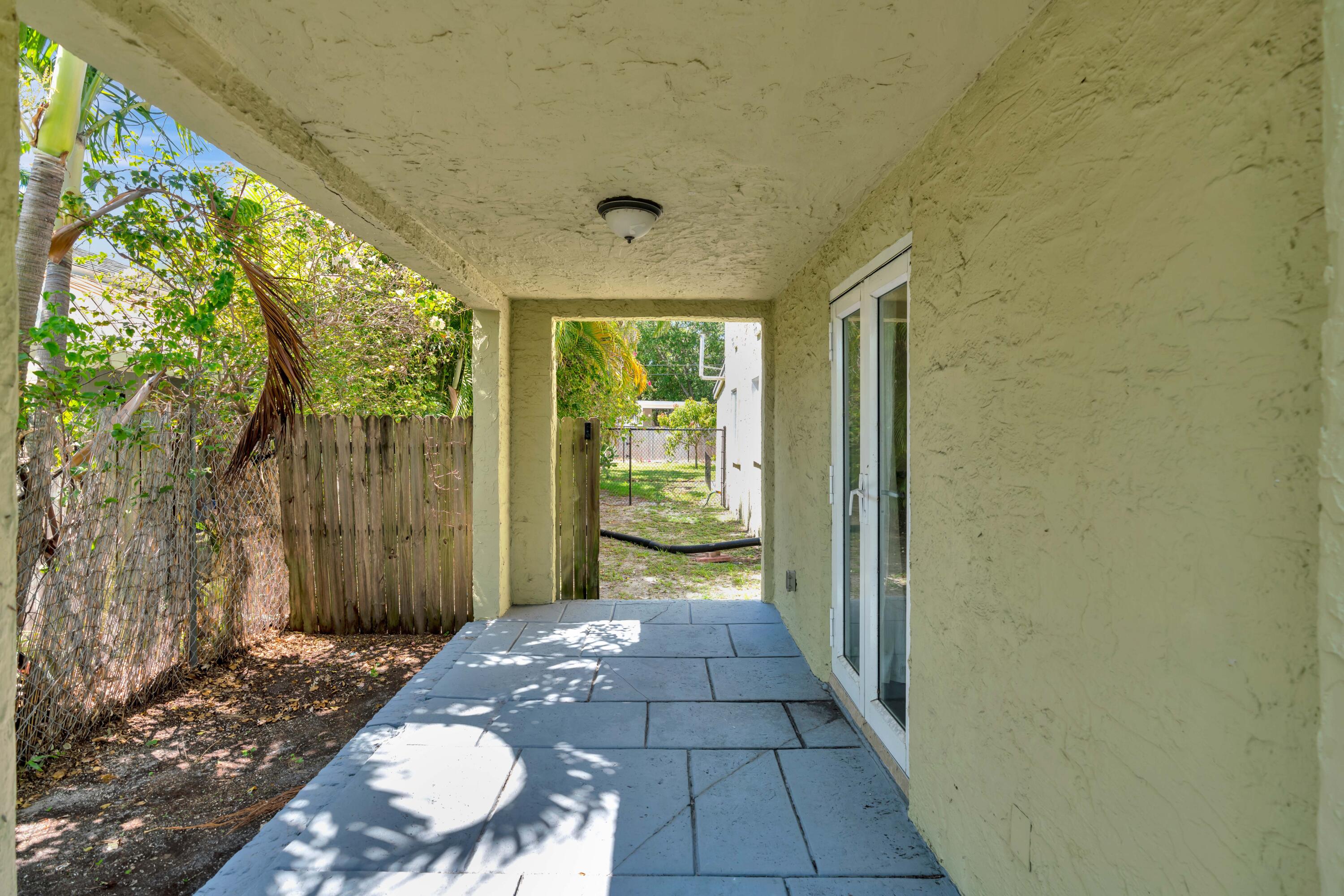 Covered patio with gray tile flooring and sliding glass doors, opening toward a leafy fenced yard.