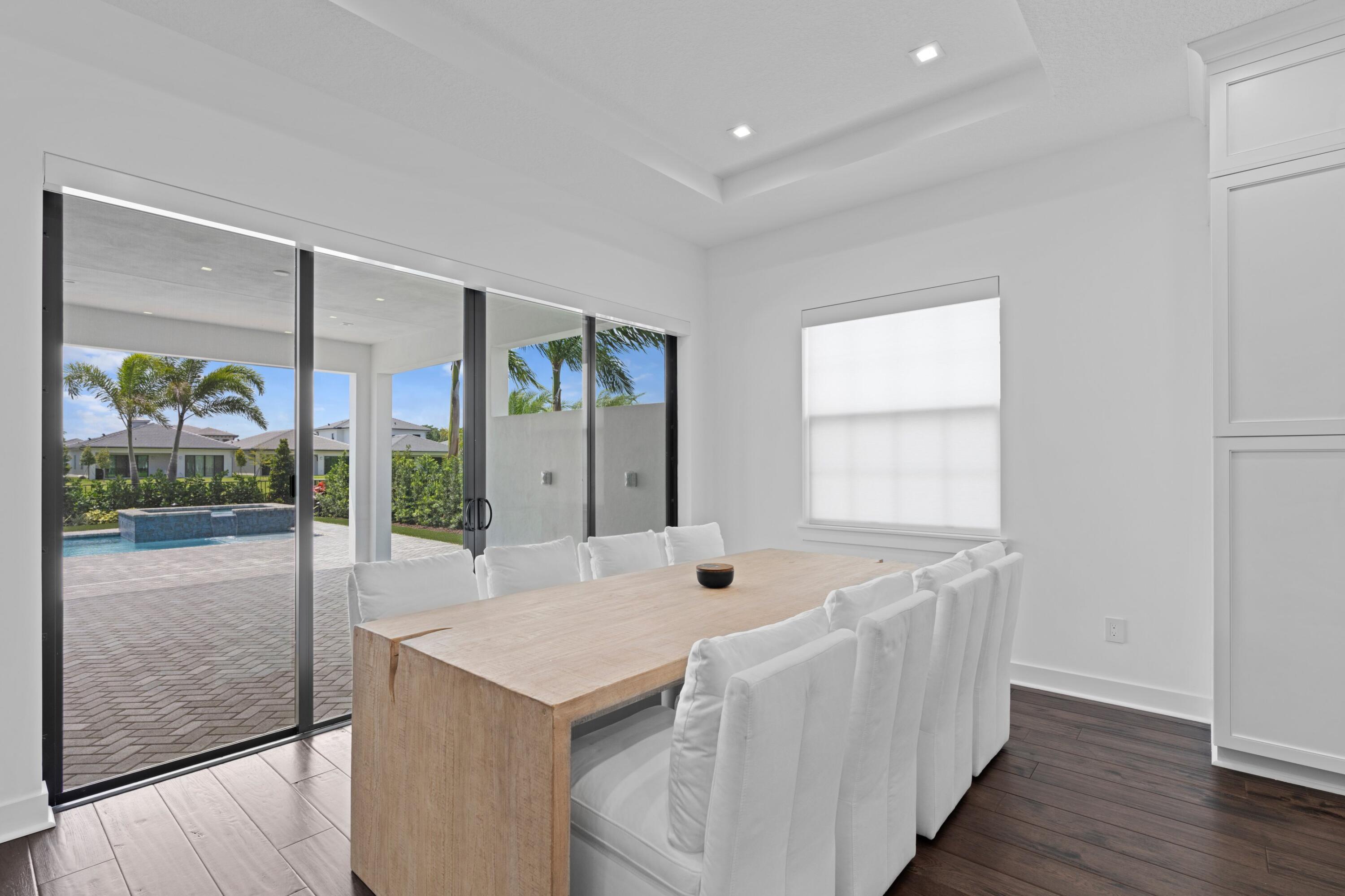 Modern dining room with a long wood table and white chairs overlooking a patio pool.