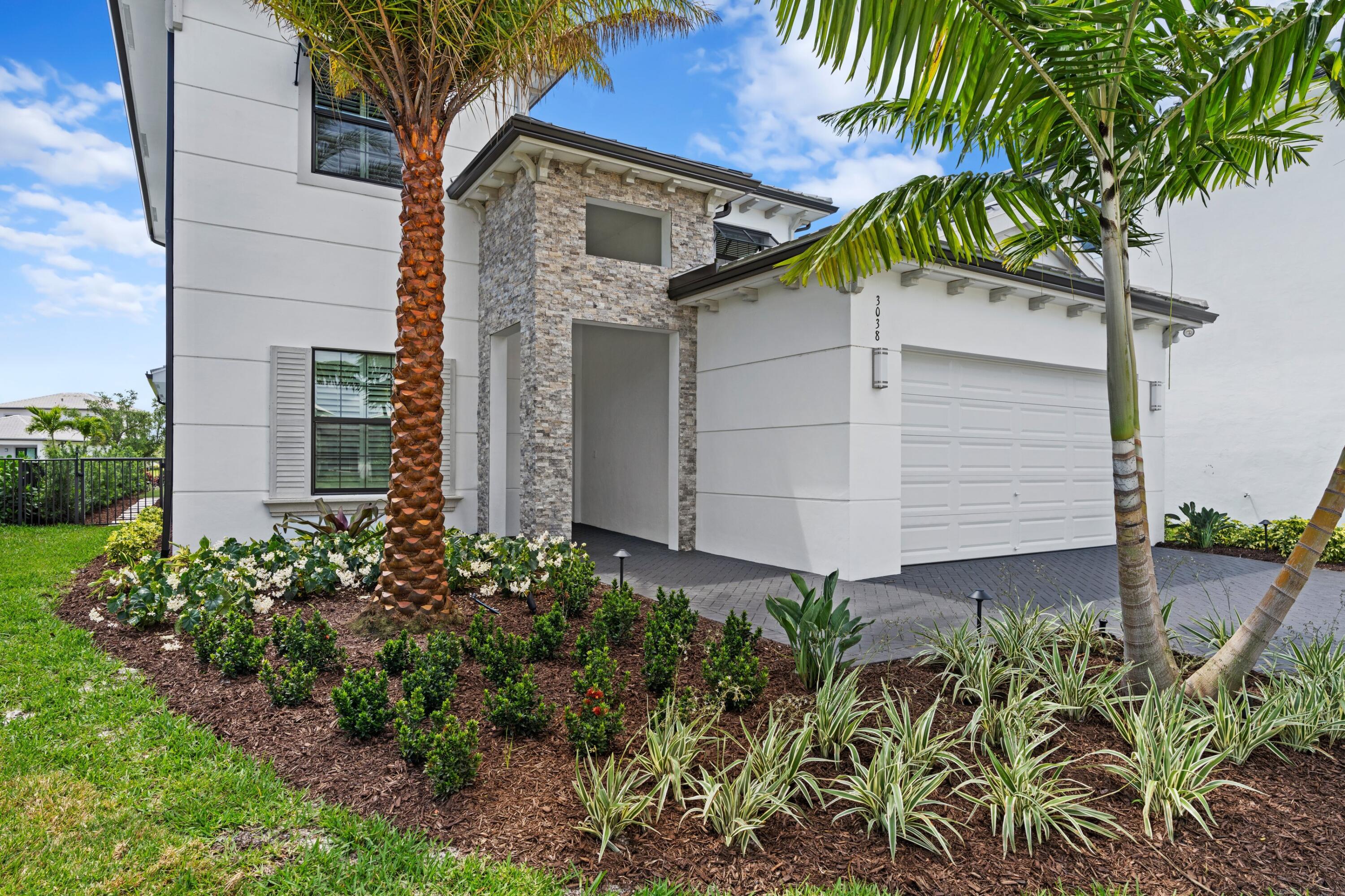 Modern white two-story home with stone entry, two-car garage, and tropical landscaping.