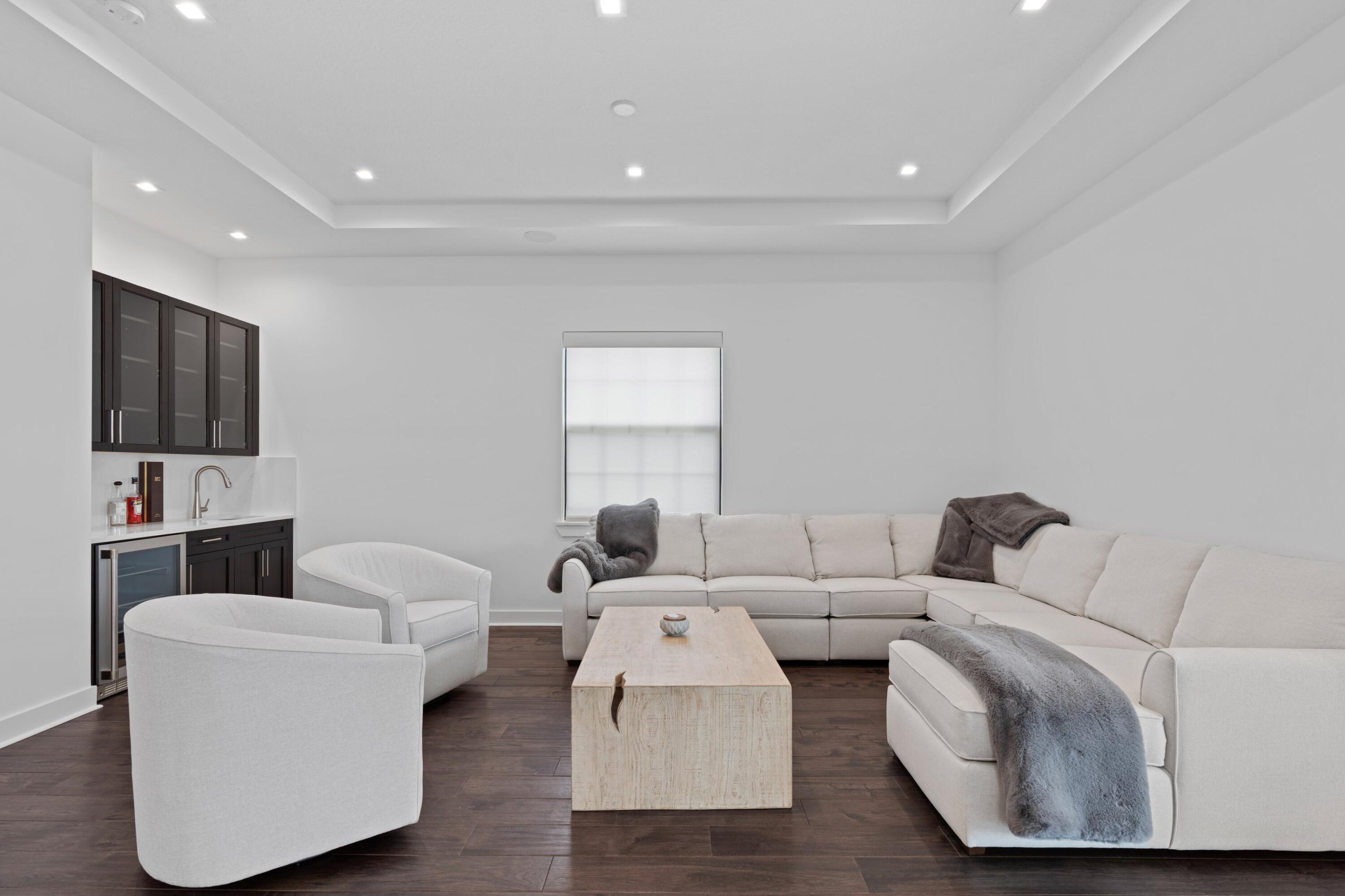 Modern living room with a cream sectional, matching armchairs, pale wood coffee table, and built-in wet bar.
