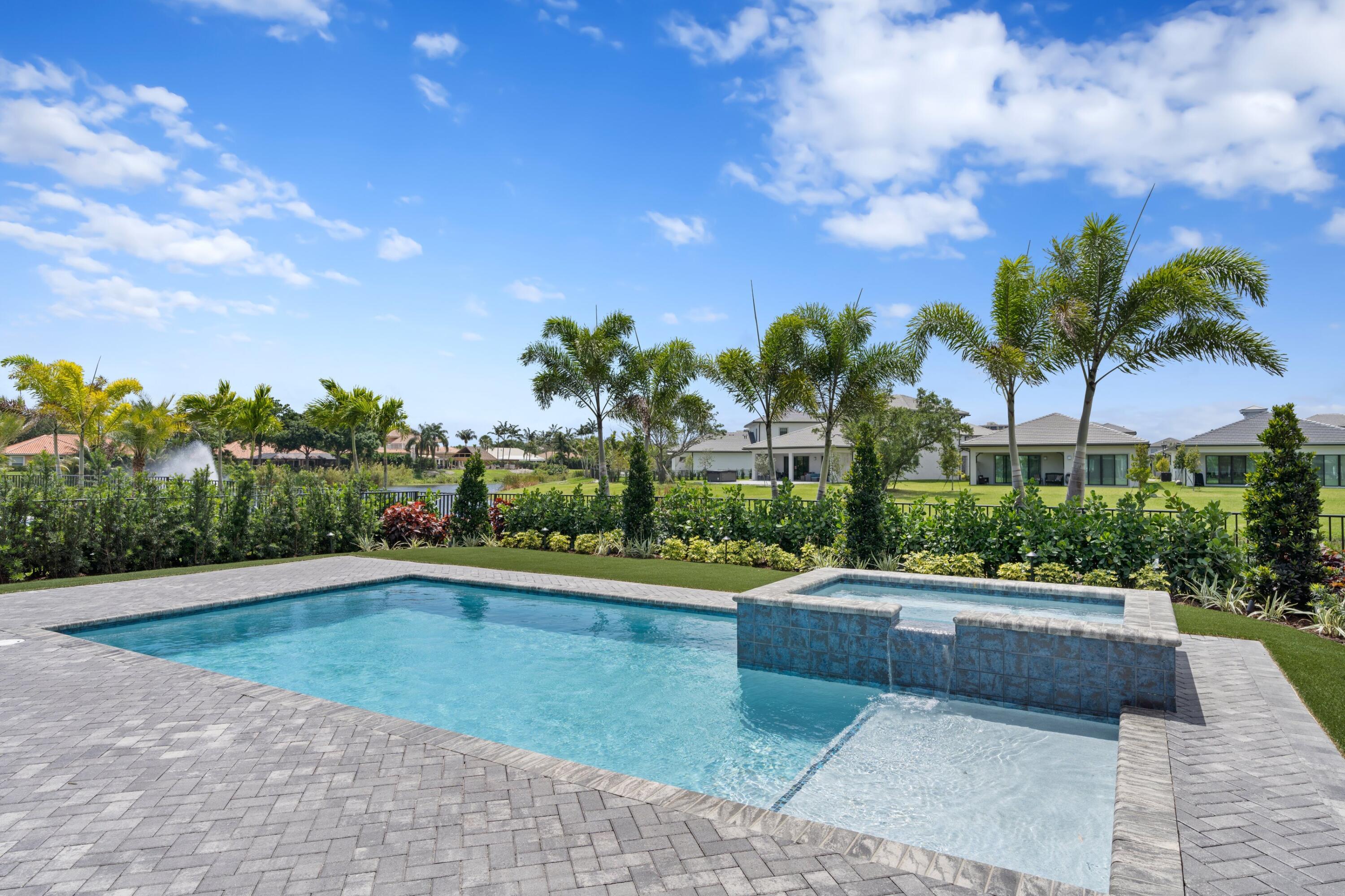 Backyard pool and raised spa bordered by gray pavers, palms, and tropical landscaping.