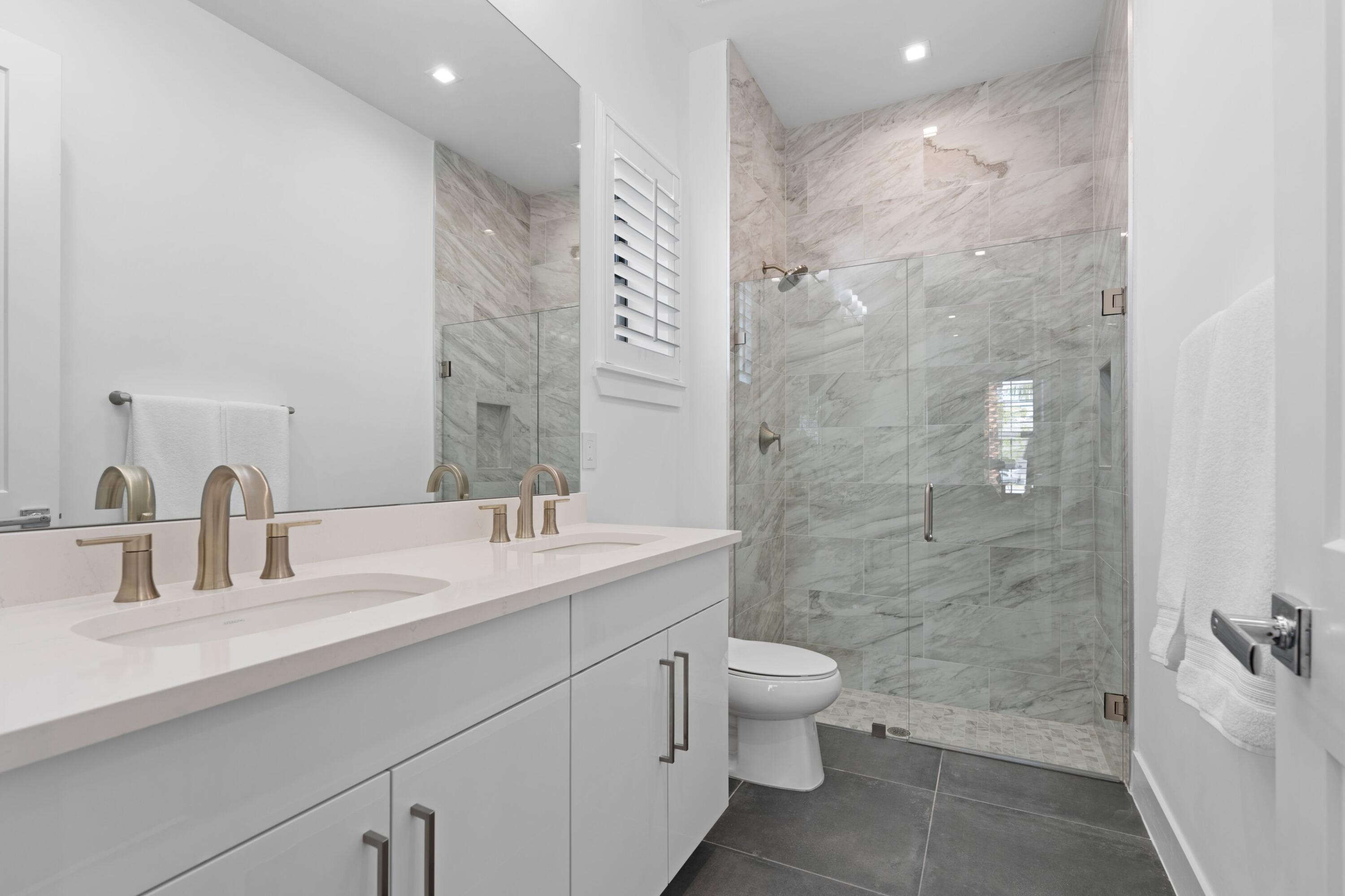 Bathroom with a double vanity and glass-enclosed marble-look walk-in shower.